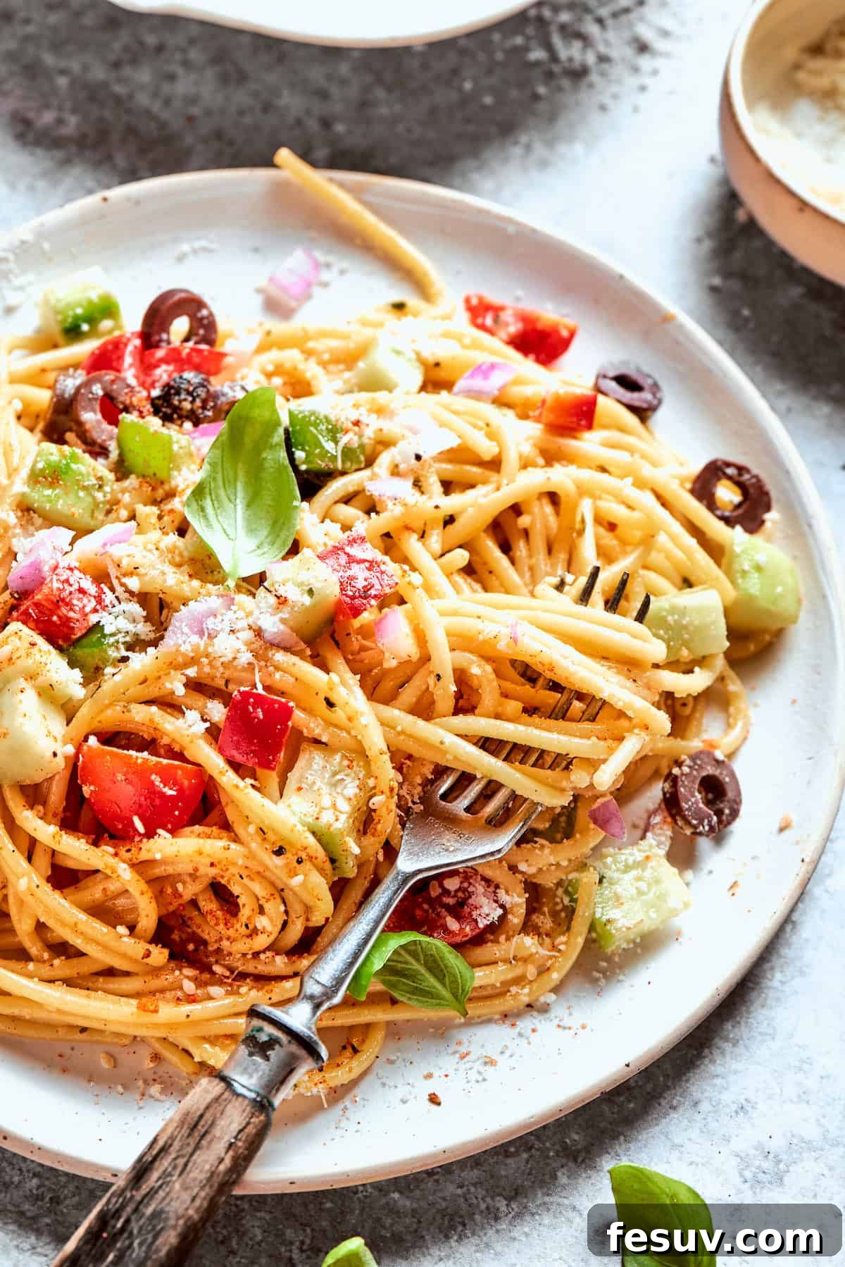 Refreshing Spaghetti Salad is loaded with summery vegetables like juicy cherry tomatoes, crunchy cucumbers, and bell peppers. A fork scoops into a plate of spaghetti salad.
