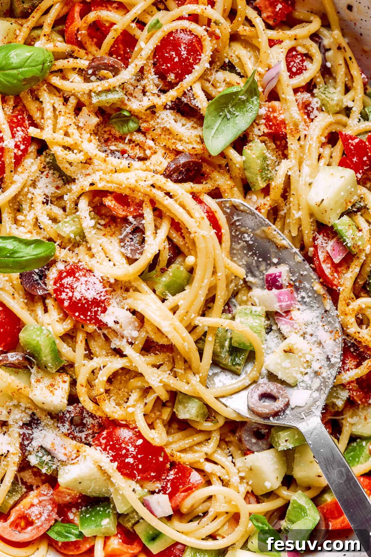 Refreshing Spaghetti Salad is loaded with summery vegetables like juicy cherry tomatoes, crunchy cucumbers, and bell peppers. A close up of spaghetti salad shows cheese, noodles, vegetables, and olives.