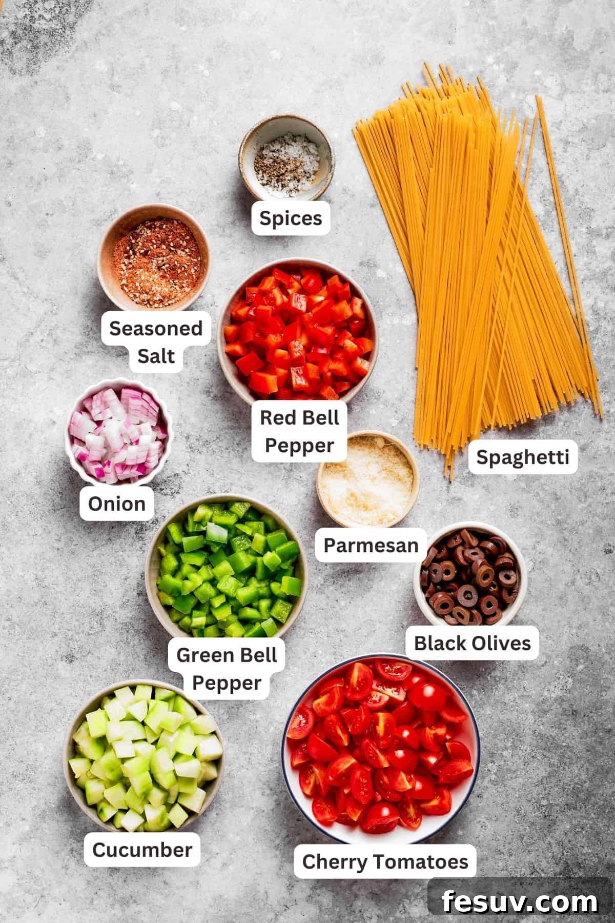 Spaghetti Salad is loaded with summery vegetables like juicy cherry tomatoes, crunchy cucumbers, and bell peppers. Ingredients for spaghetti salad are labeled and portioned out: spaghetti, cucumber, tomatoes, onion, bell peppers, black olives, parmesan.