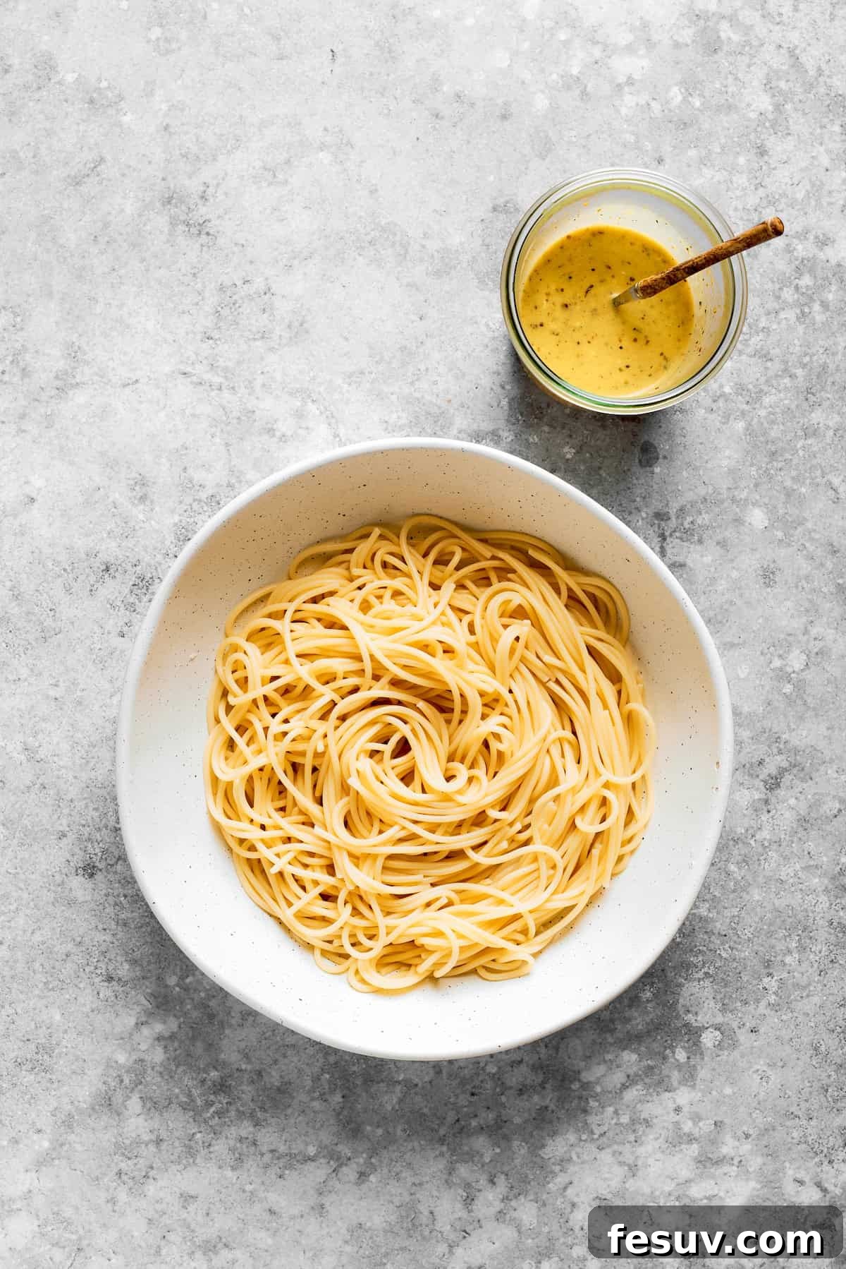 Refreshing Spaghetti Salad is loaded with summery vegetables like juicy cherry tomatoes, crunchy cucumbers, and bell peppers. The spaghetti is placed in a bowl with the dressing next to it.