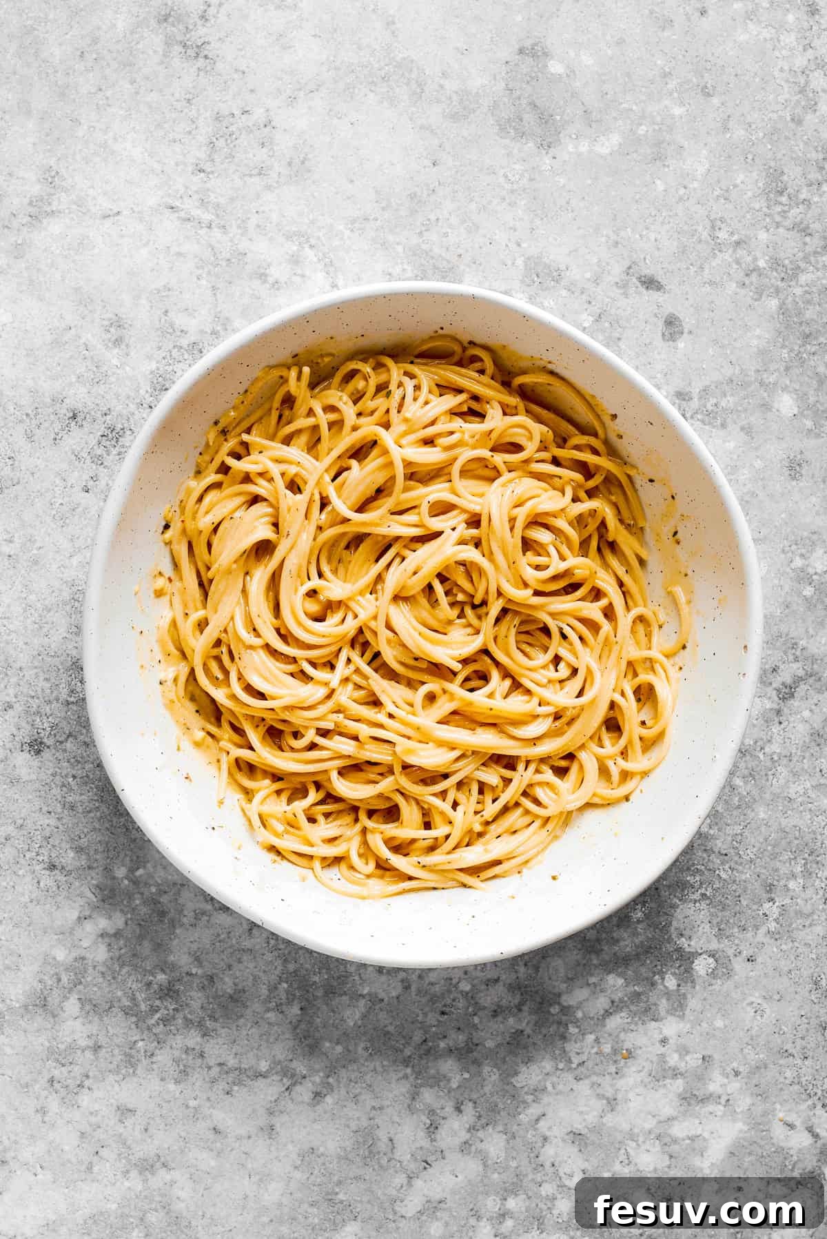 Refreshing Spaghetti Salad is loaded with summery vegetables like juicy cherry tomatoes, crunchy cucumbers, and bell peppers. Cooked spaghetti noodles in a white bowl.