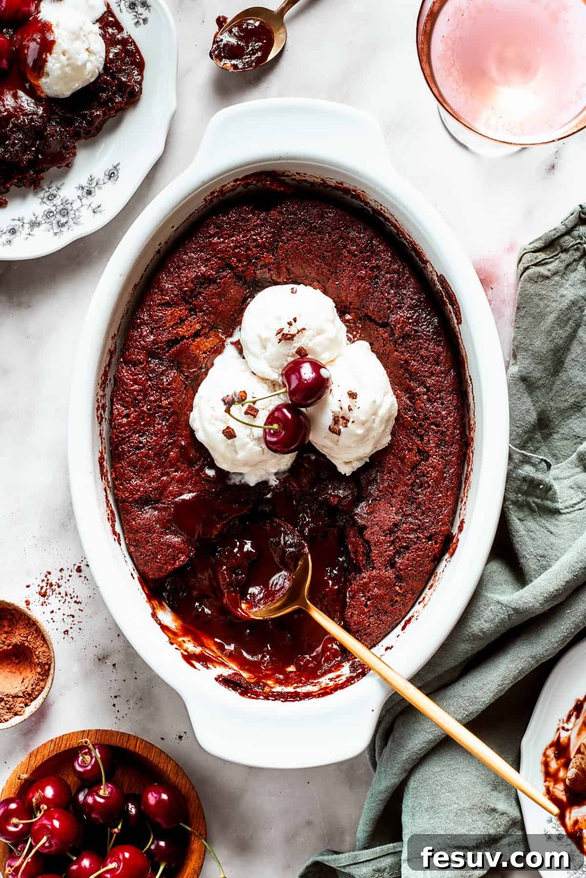 Heavenly Chocolate Pudding Cake 14 Chocolate cake in a casserole dish garnished with vanilla ice cream scoops, two cherries, with a gold-colored spoon set inside the cake.