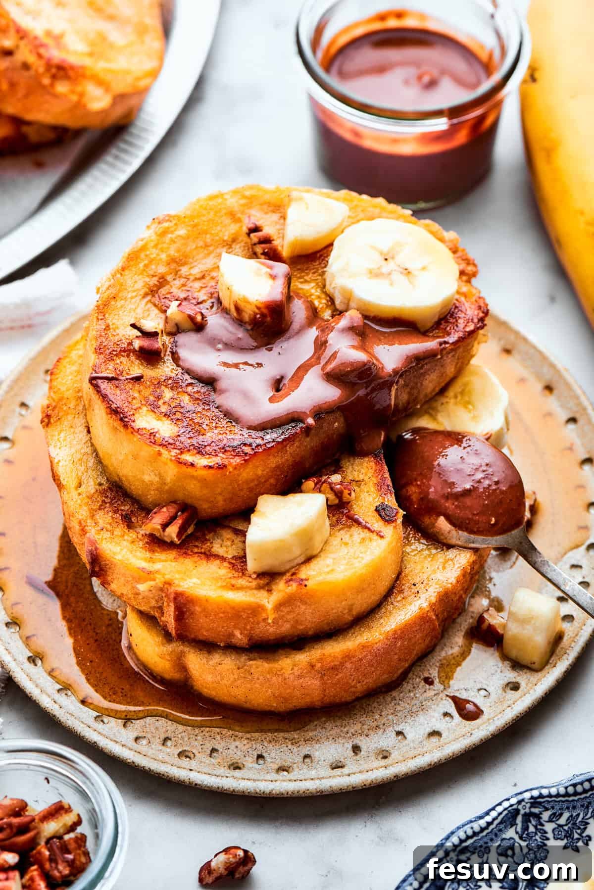 Delectable Banana French Toast, golden brown and garnished with fresh fruit and spread. Three slices of banana French toast are artfully stacked on a plate, generously topped with fresh banana slices and a rich swirl of chocolate hazelnut spread.