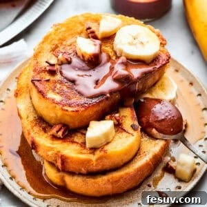 Three slices of French toast are stacked on top of each other on a plate and topped with banana slices and Nutella.