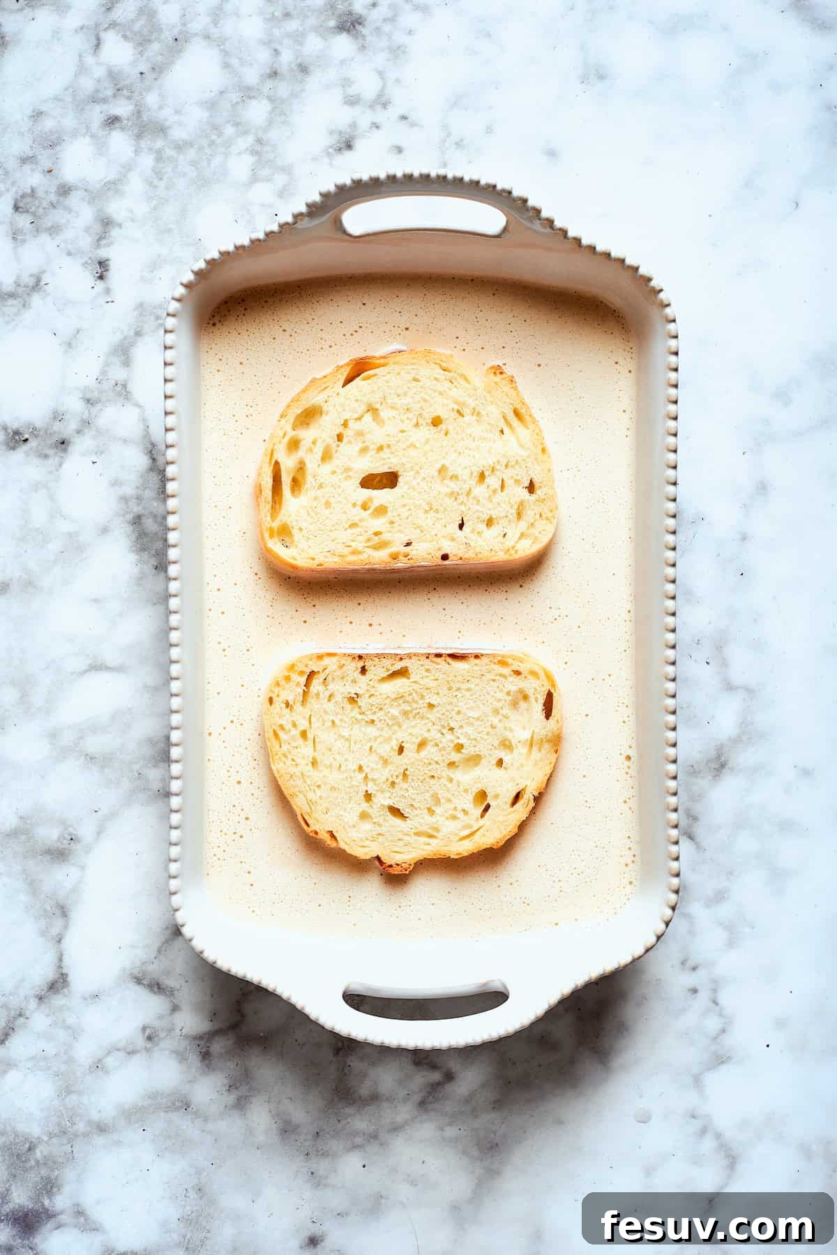 Soaking bread slices in the banana mixture. Two thick slices of bread are gently soaking in the rich banana-infused batter, ensuring they absorb all the delicious flavors before cooking.