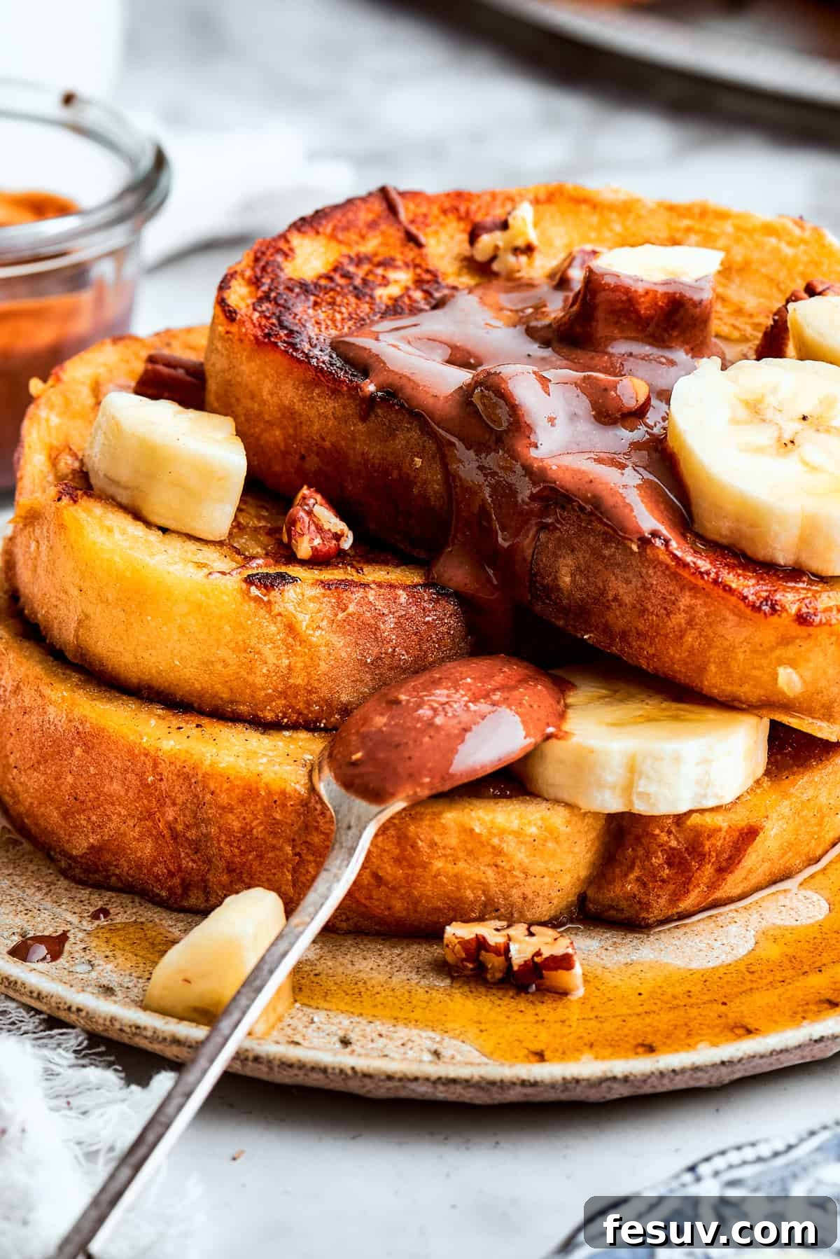 Close-up of Banana French Toast with chocolate spread and banana slices. A close-up view of a perfectly stacked tower of golden-brown French toast, beautifully garnished with delicate slices of fresh banana and a rich, swirling pattern of chocolate hazelnut spread, highlighting the inviting textures and flavors.
