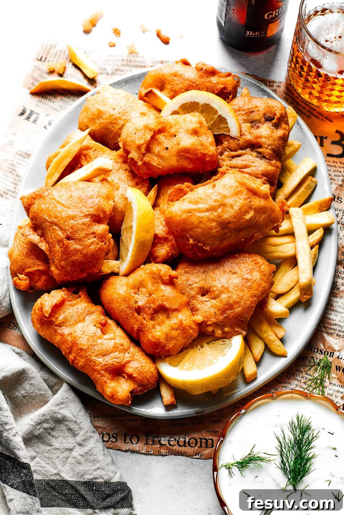 Pieces of golden brown fried fish are artfully arranged on a platter over a bed of crispy French fries, ready to be served.