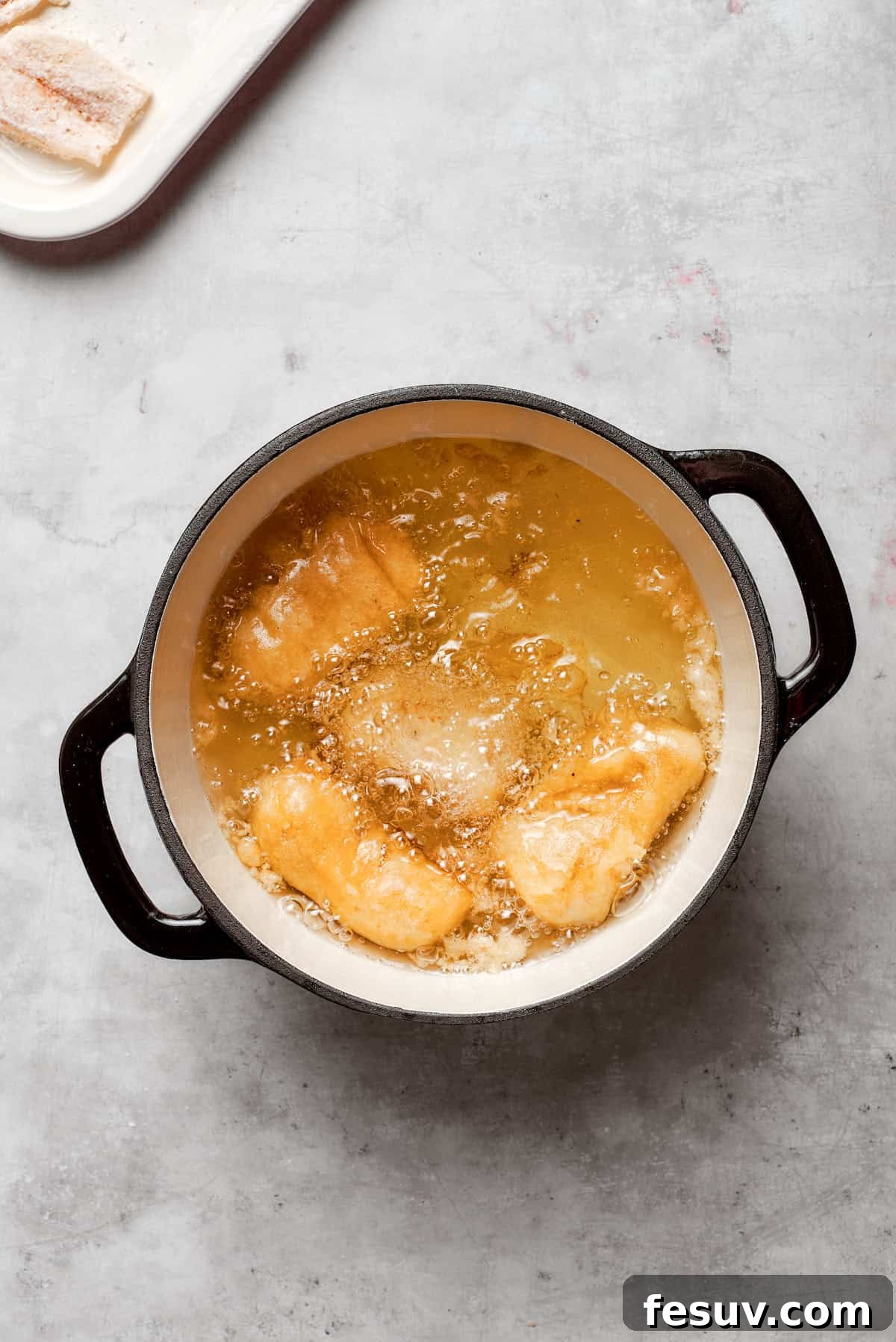 Pieces of beer-battered fish are frying in a pot of hot oil, bubbling to a golden crisp.