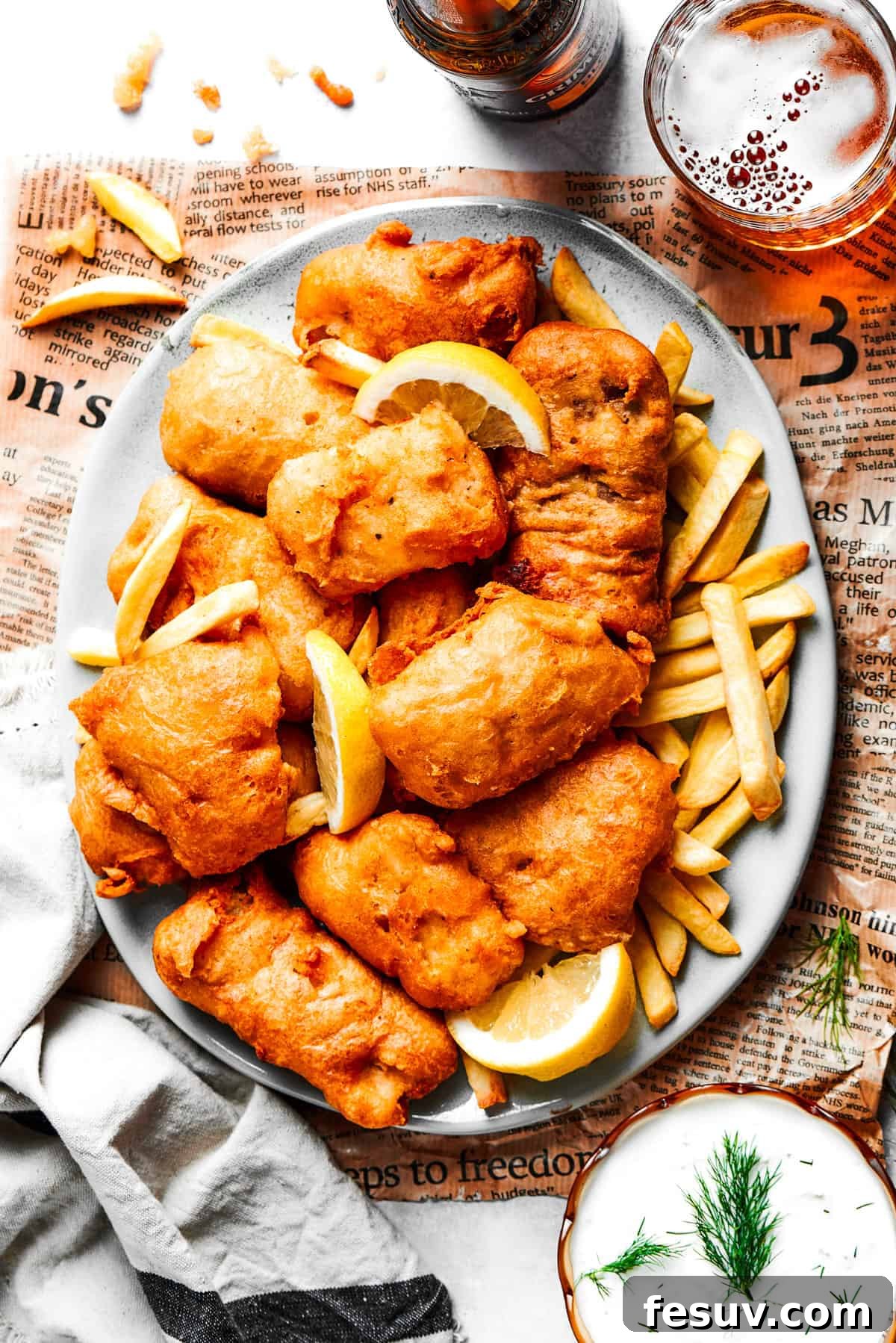 An overhead view of a platter filled with freshly fried beer-battered fish, golden French fries, and a bowl of creamy tartar sauce.
