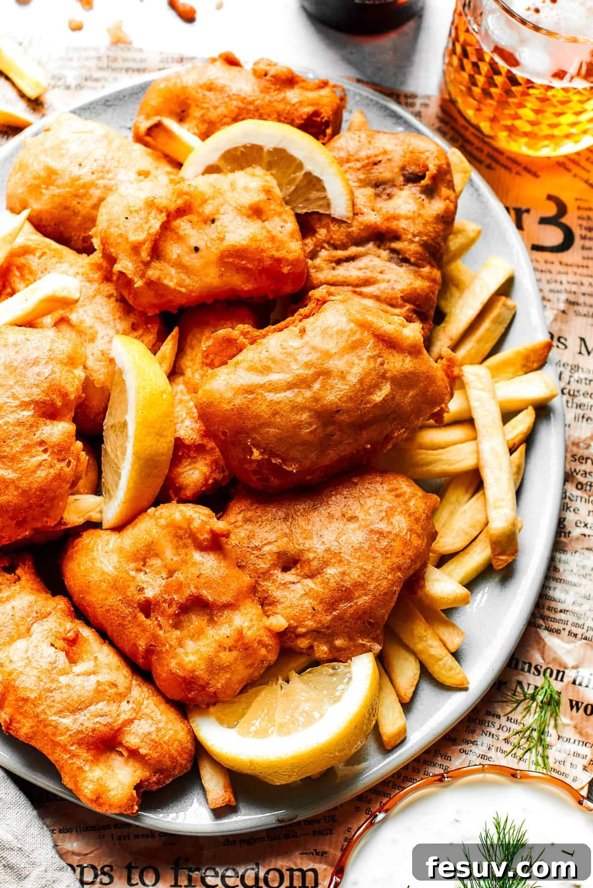 A large platter presenting golden beer-battered fish and a heap of French fries, garnished with lemon wedges.