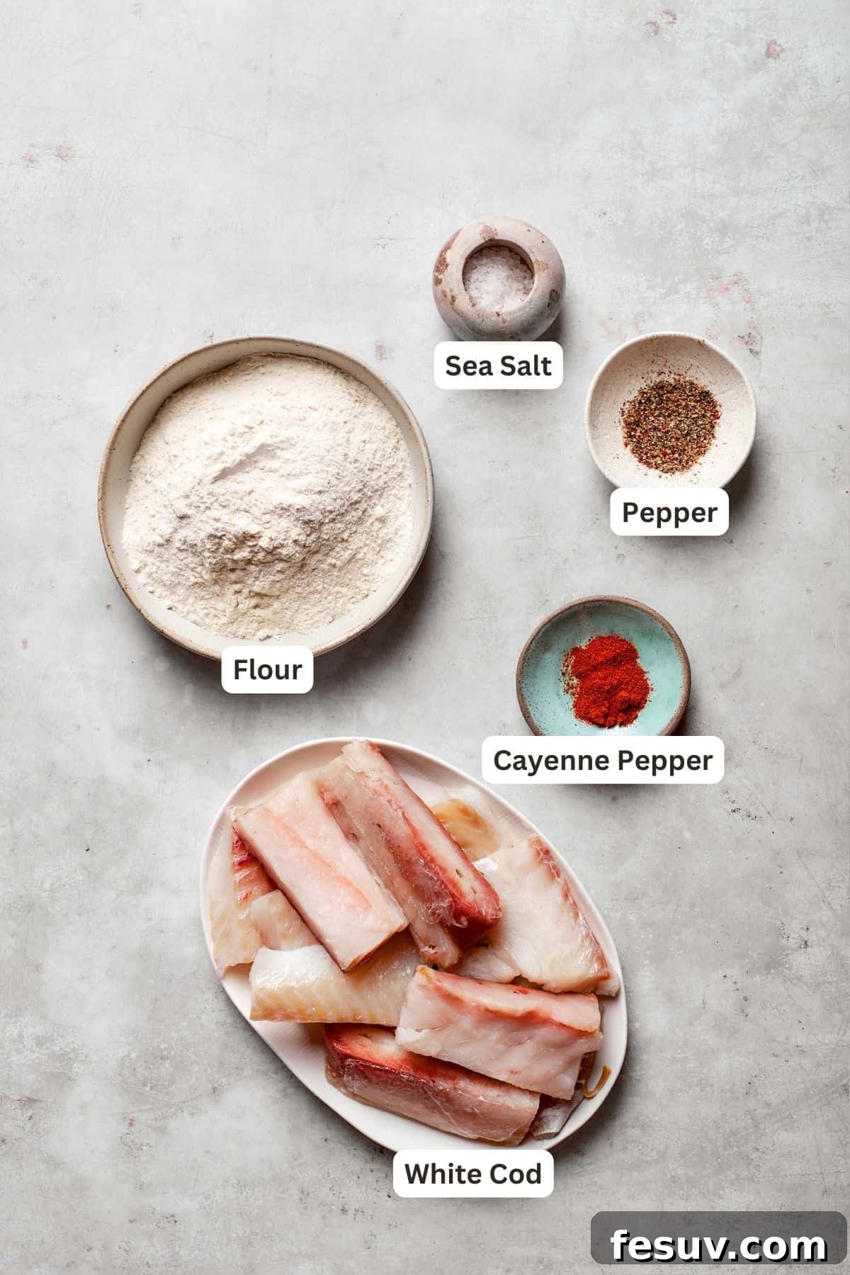 A selection of fresh ingredients including white fish, flour, spices, and a bottle of light beer, laid out on a wooden surface.