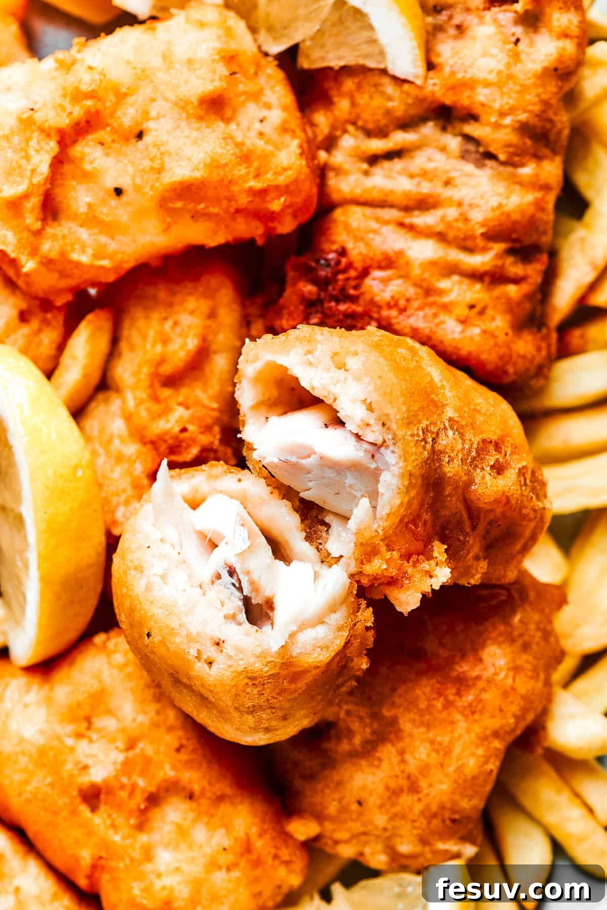 A perfectly fried piece of beer battered fish, cut in half to reveal its flaky white interior and crisp golden crust.
