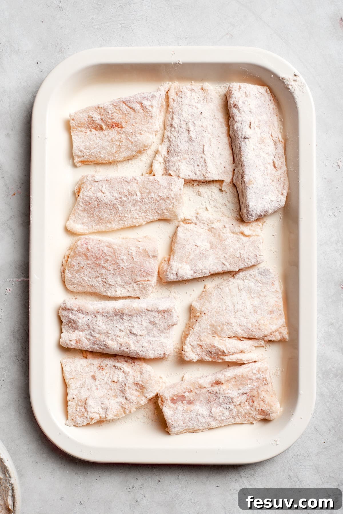 Several floured fish pieces are neatly arranged on a baking tray, ready for the next step.