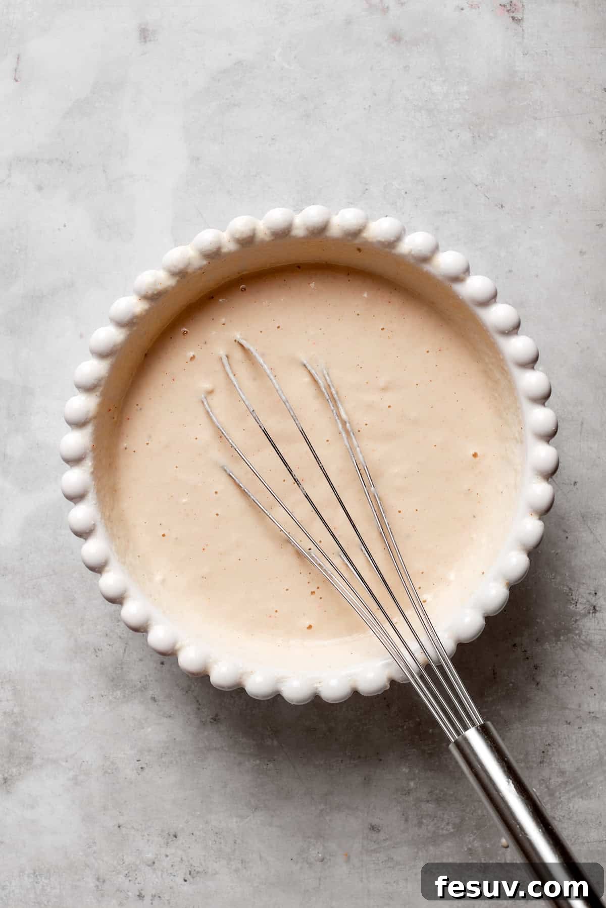 A whisk is actively mixing cold beer into the dry batter ingredients in a bowl.
