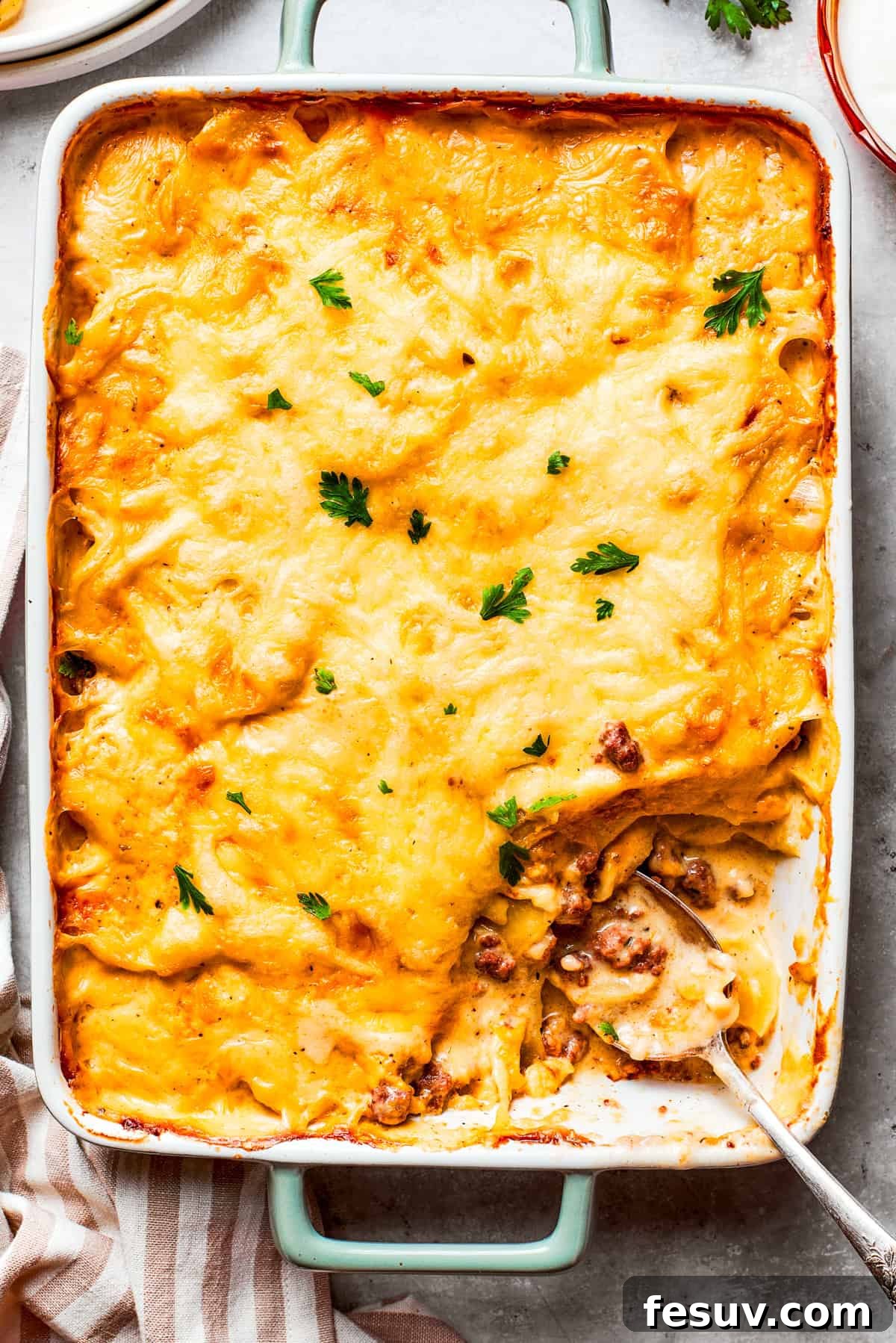 Hearty Hamburger Potato Casserole with layers of savory ground beef, thinly sliced Yukon gold potatoes, creamy mushroom soup, and a golden melted cheese topping. A warm, inviting Hamburger Potato Casserole in a baking dish, with a serving portion gently removed from the corner, revealing its delightful layers of ground beef, potatoes, and cheese.