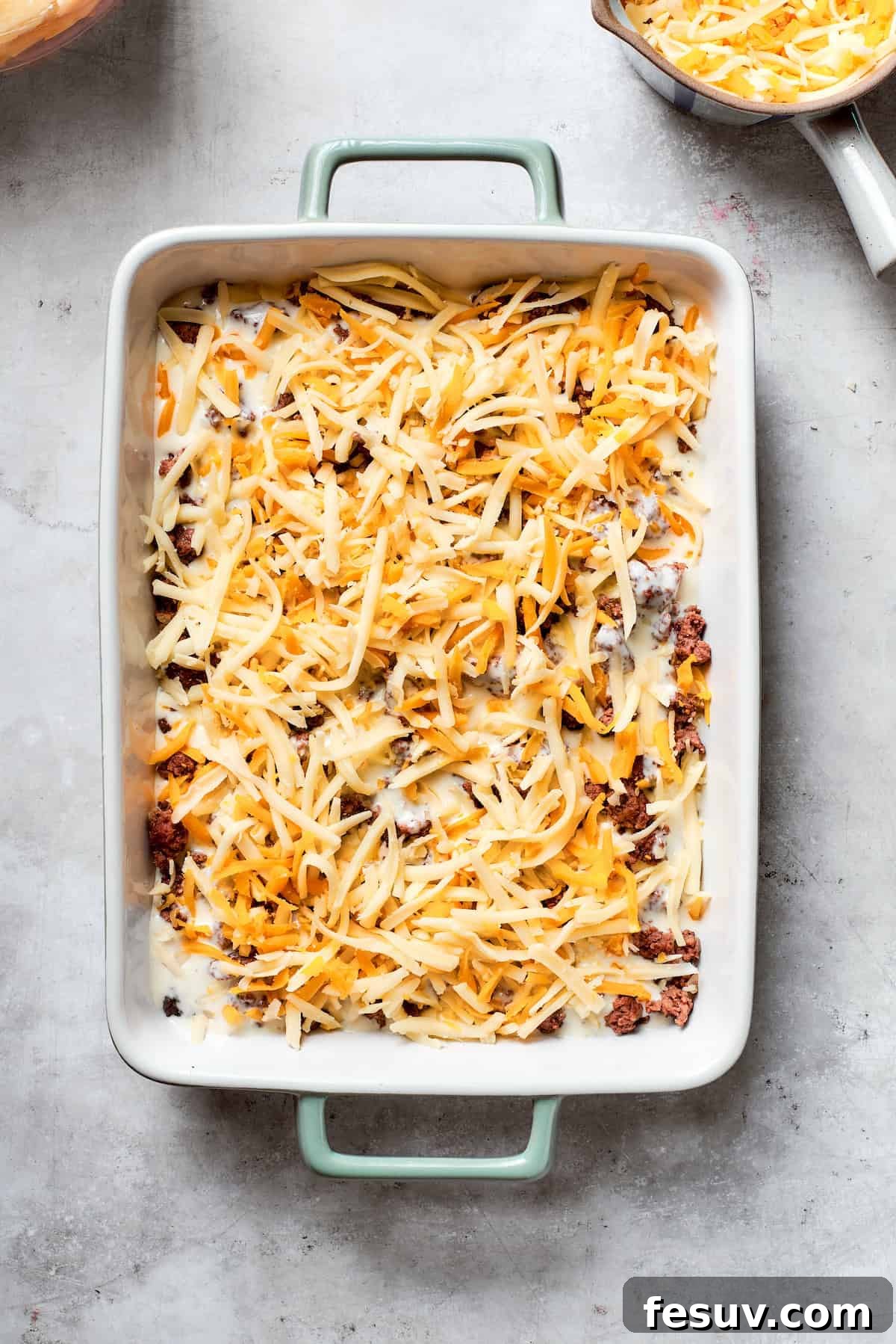 Hearty Beef & Potato Bake 6 Shredded cheese is generously sprinkled over a layer of cooked ground beef in the casserole dish, preparing for the next layer.