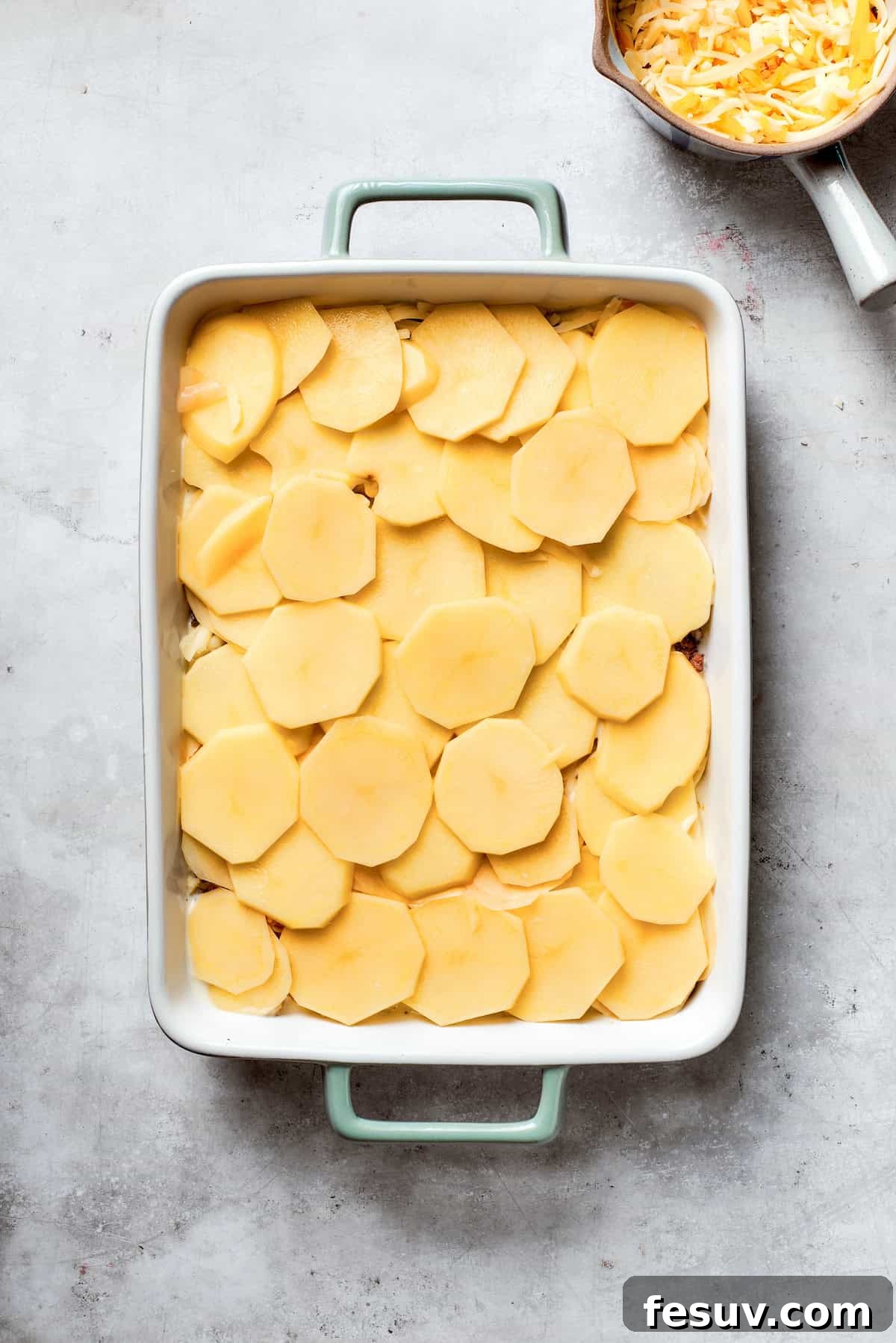 Hearty Beef & Potato Bake 7 Another layer of thinly sliced potatoes is added over the cheese and beef, continuing the precise layering process for the casserole.