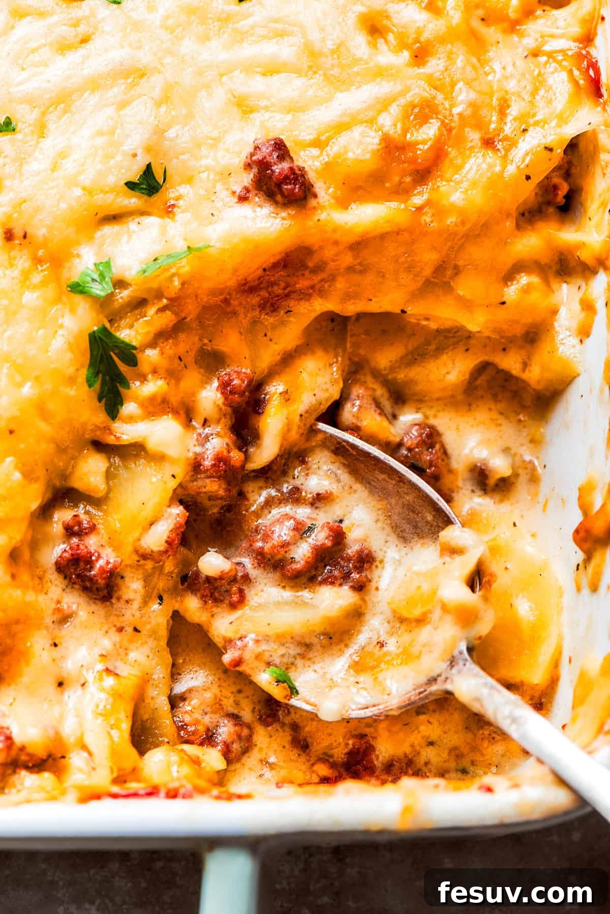 Creamy Hamburger Potato Casserole with savory ground beef and tender sliced potatoes. A spoon gently scoops into a freshly baked Hamburger Potato Casserole, showing the creamy texture and layers of ground beef and potatoes, ready to be served.