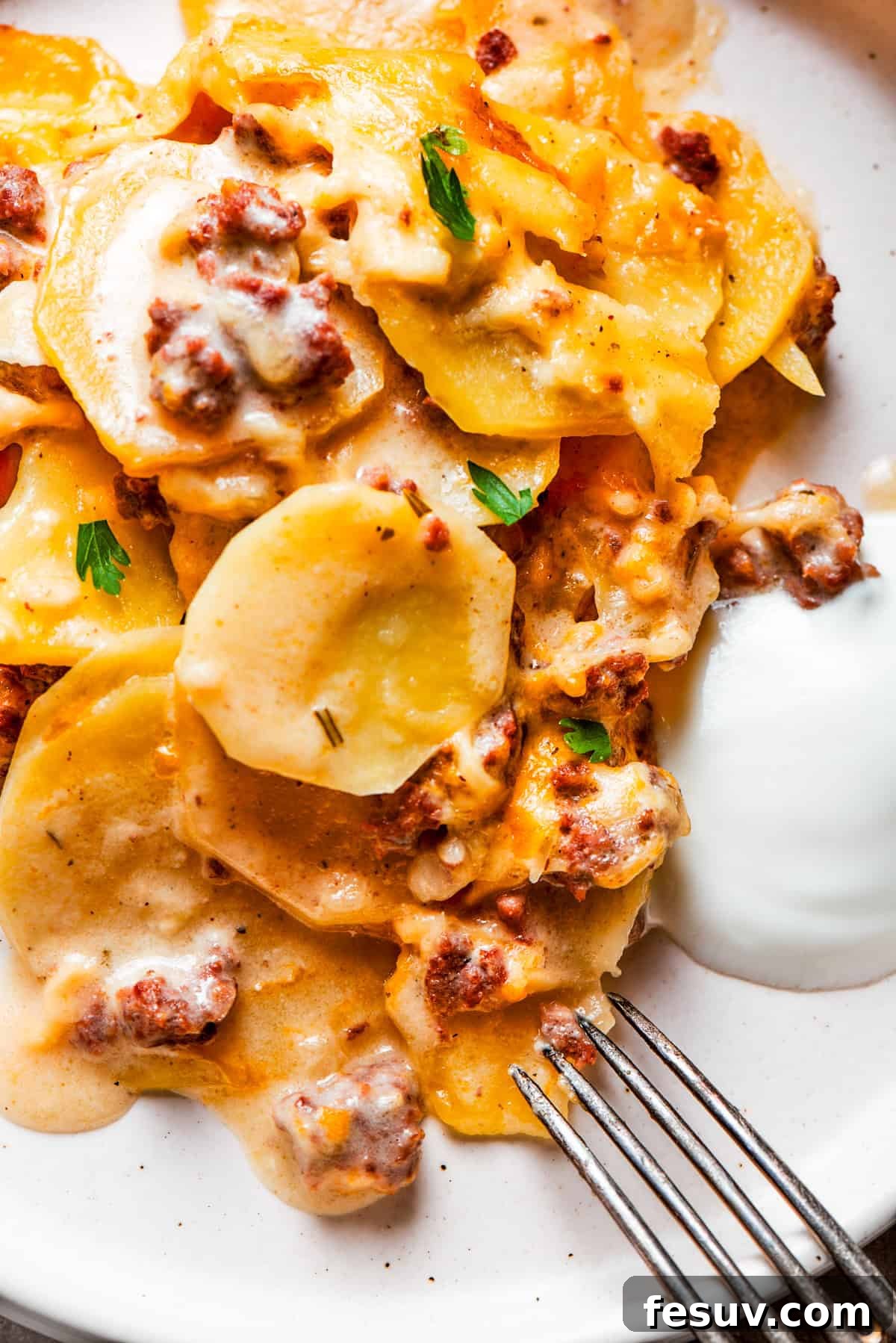 A serving of Hamburger Potato Casserole on a dinner plate, with a fork. A close-up shot of a single serving of cooked Hamburger Potato Casserole on a dinner plate, showcasing the tender sliced potatoes, savory ground beef, and melted cheese, with a fork poised next to it.
