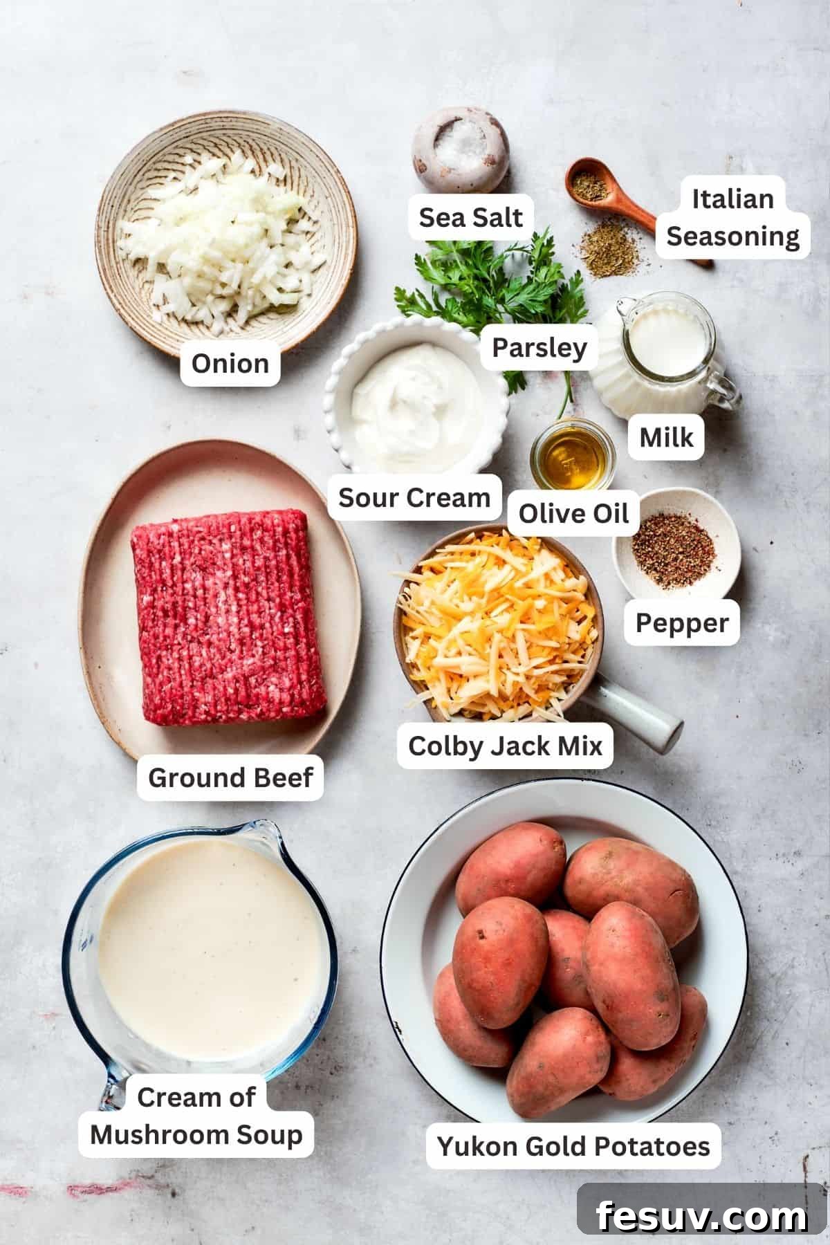 Key Ingredients for Hamburger Potato Casserole: ground beef, Colby Jack cheese, onion, sour cream, milk, Italian seasoning, cream of mushroom soup, and Yukon gold potatoes. All the essential ingredients for hamburger potato casserole are neatly arranged: ground beef, a blend of Colby Jack cheese, a whole yellow onion, sour cream, salt, black pepper, milk, Italian seasoning, cream of mushroom soup, and thinly sliced Yukon gold potatoes.