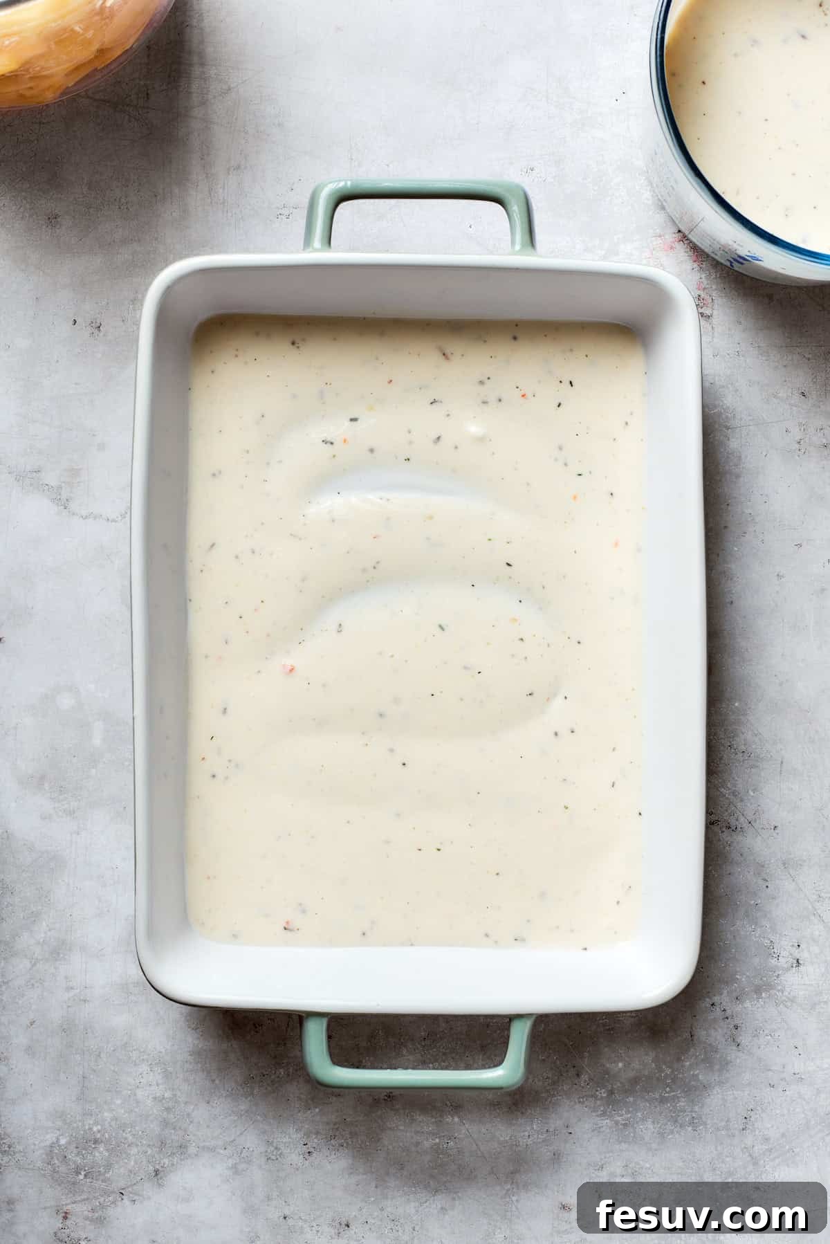 Hearty Beef & Potato Bake 4 A small amount of the creamy mushroom soup mixture is spread evenly across the bottom of a greased baking dish, forming the base layer.