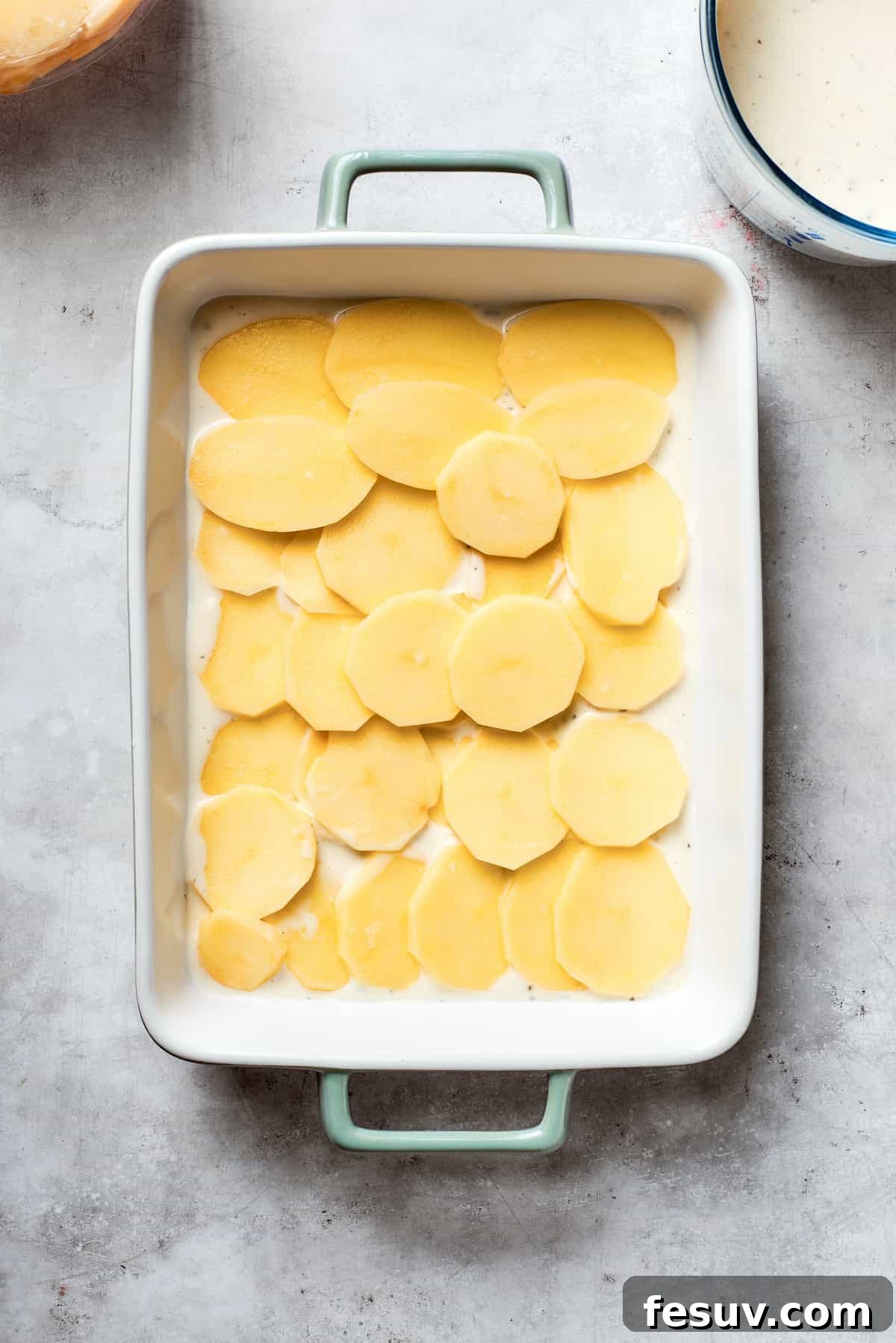 Hearty Beef & Potato Bake 5 Thinly sliced potatoes are meticulously arranged in a single, even layer over the soup mixture at the bottom of the baking pan.