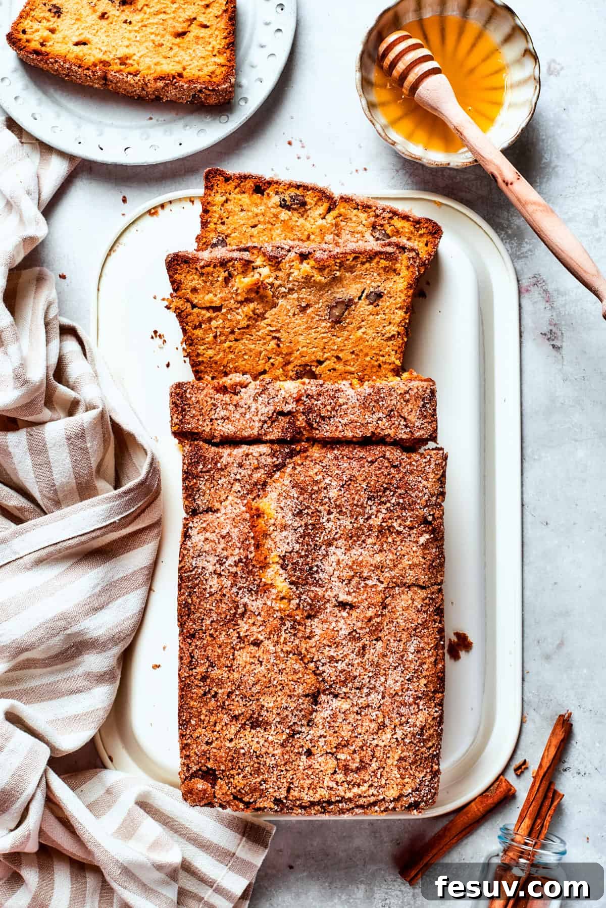 A serving platter holds a loaf of Amish friendship bread with a slice cut out, next to a small bowl of honey for drizzling.