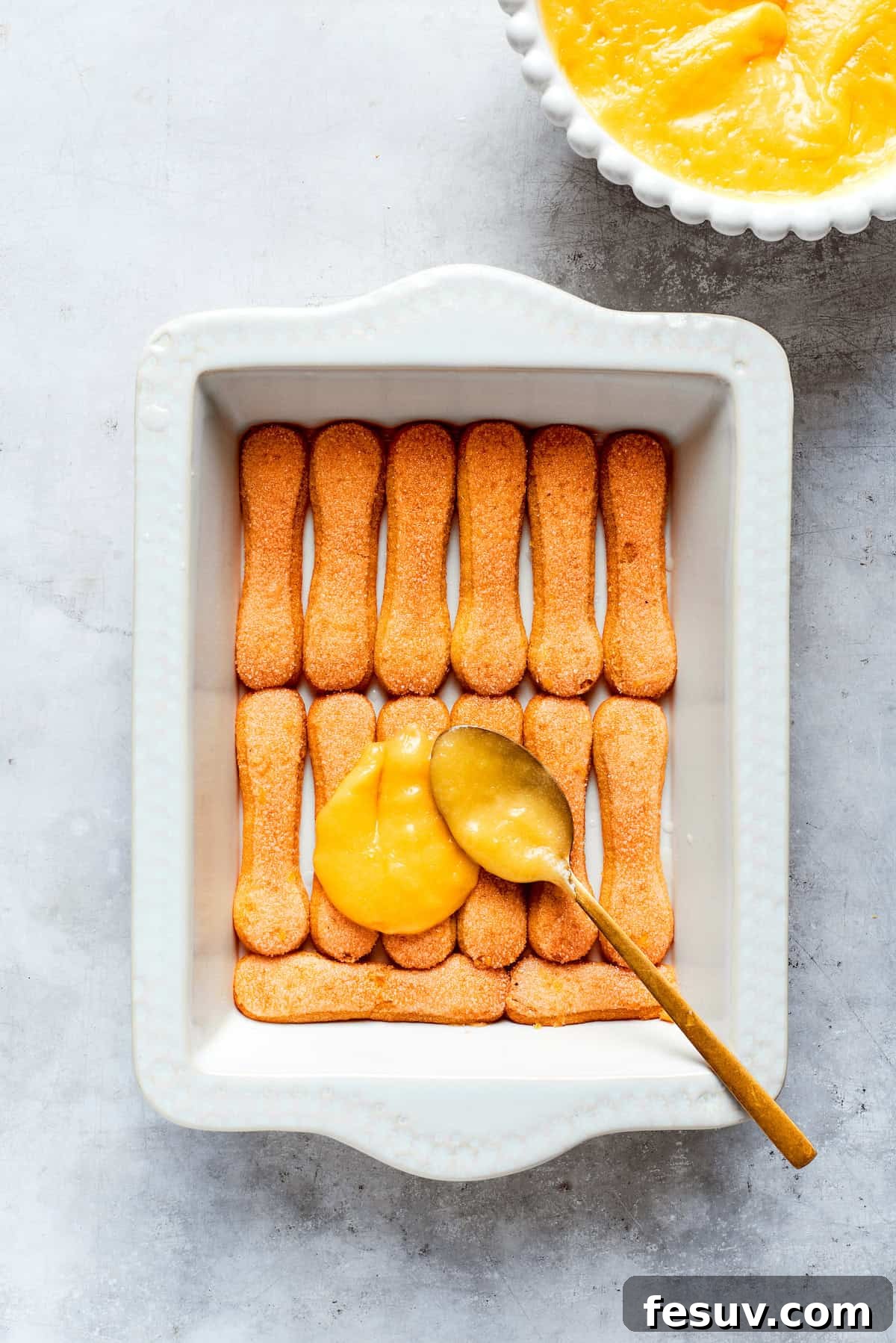 Sun-Kissed Lemon Tiramisu 15 A vibrant layer of homemade lemon curd being smoothly spread over the soaked ladyfinger cookies in the baking dish.