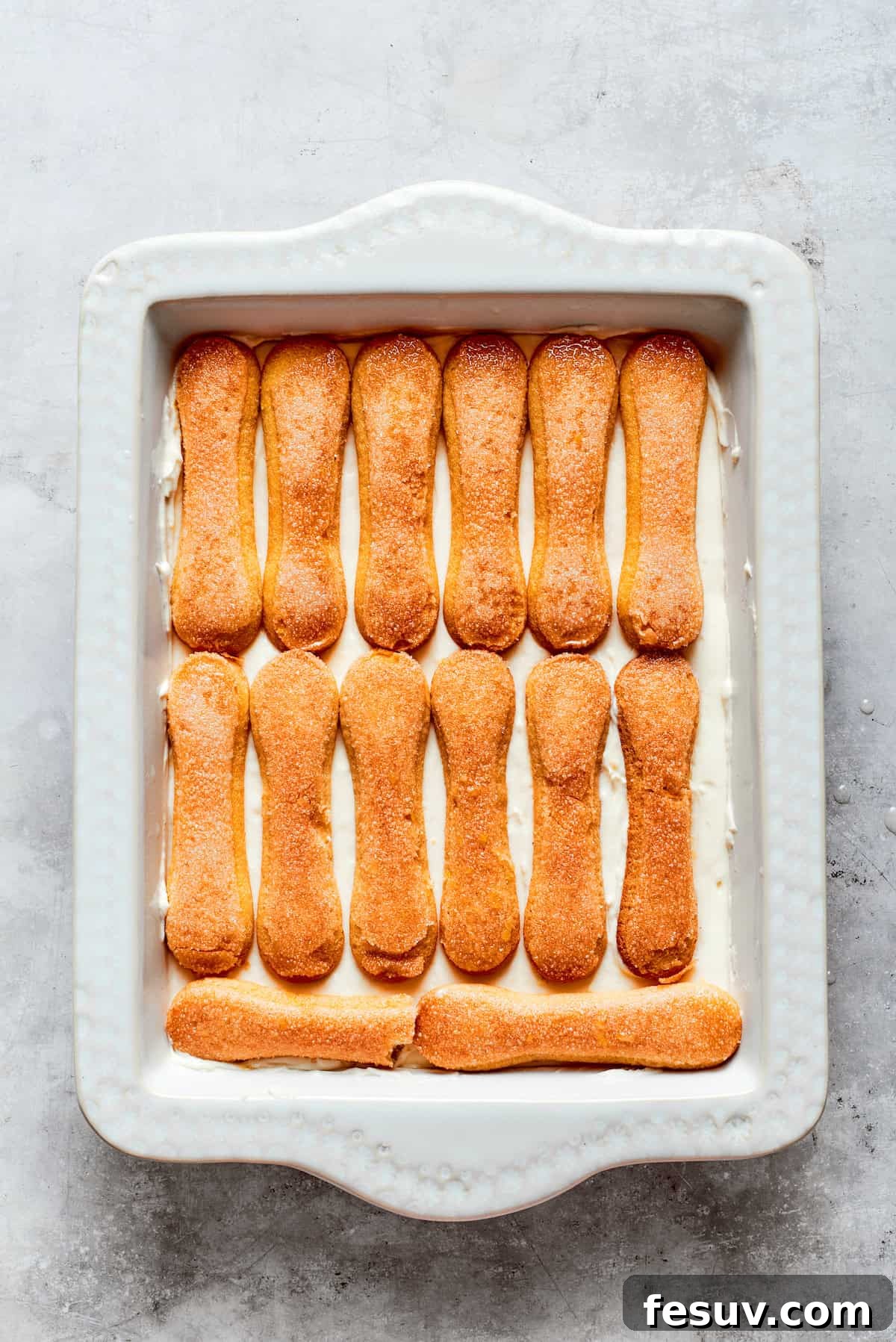 Sun-Kissed Lemon Tiramisu 17 A second layer of lemon syrup-soaked ladyfinger cookies being carefully placed over the mascarpone cream in the baking dish.