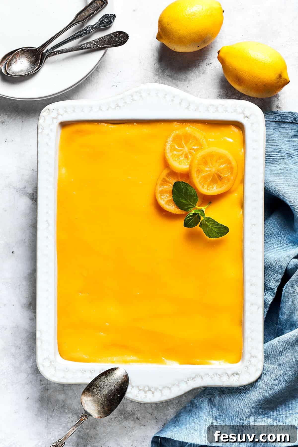 Sun-Kissed Lemon Tiramisu 19 An overhead view of a beautifully assembled lemon tiramisu in a dish, with fresh lemons arranged beside it for garnish.