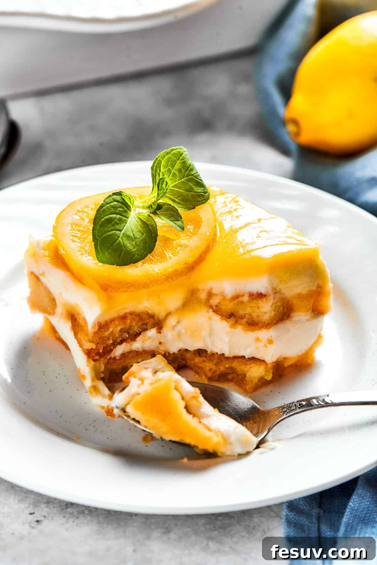 Sun-Kissed Lemon Tiramisu 21 A fork cuts into a serving of lemon tiramisu on a small dessert plate, showing the distinct layers.