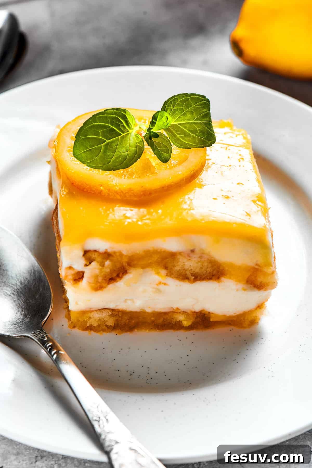 Sun-Kissed Lemon Tiramisu 7 A perfectly portioned square of lemon tiramisu, garnished with a fresh basil leaf, served on a pristine white plate.