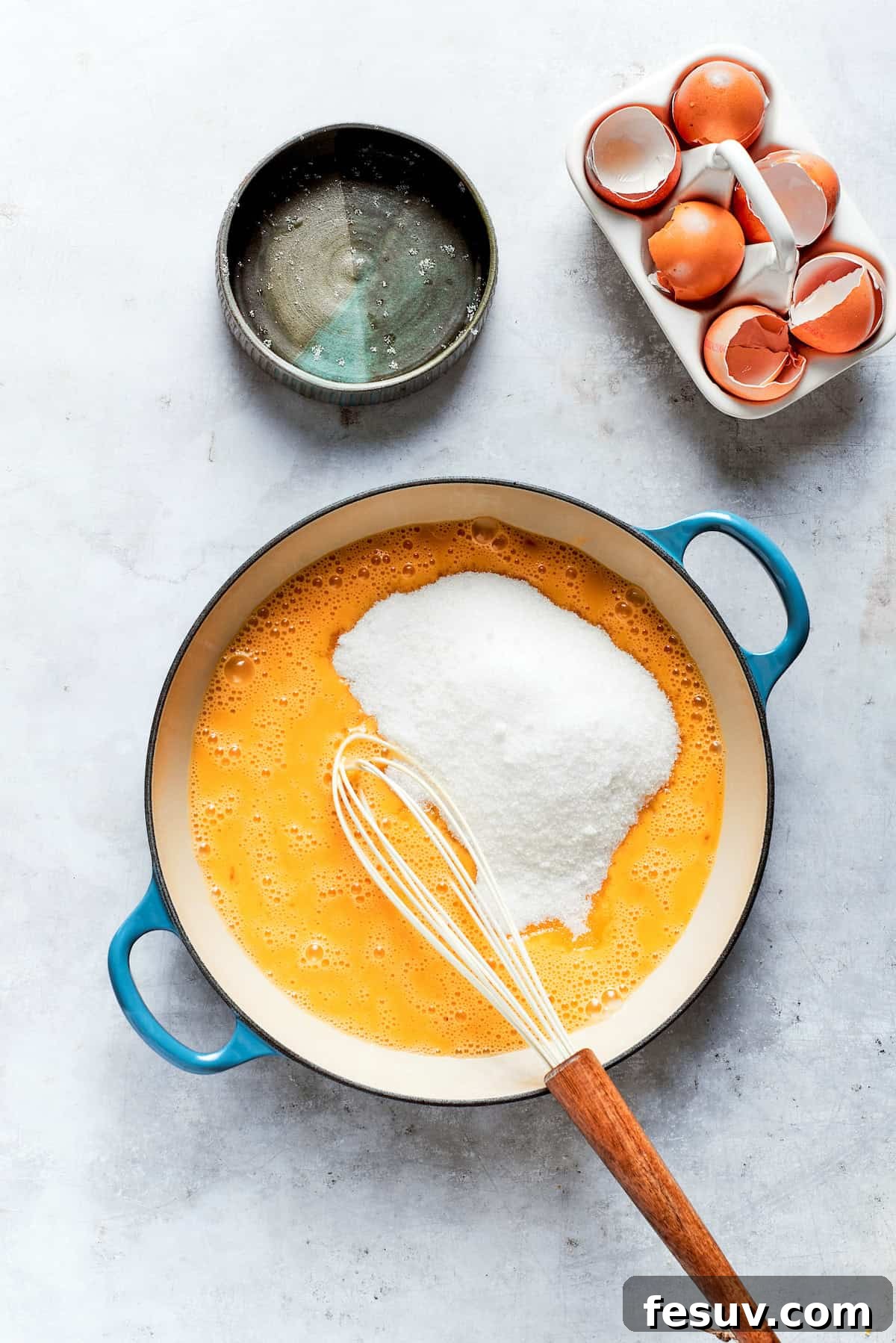 Sun-Kissed Lemon Tiramisu 10 Granulated sugar being whisked into a mixture of lemon juice and eggs in a bowl over a gentle heat.