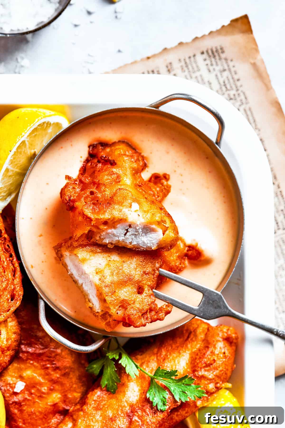 A beautifully arranged platter of beer battered chicken, accompanied by a glass of beer and a bowl of dipping sauce, ready to be served.