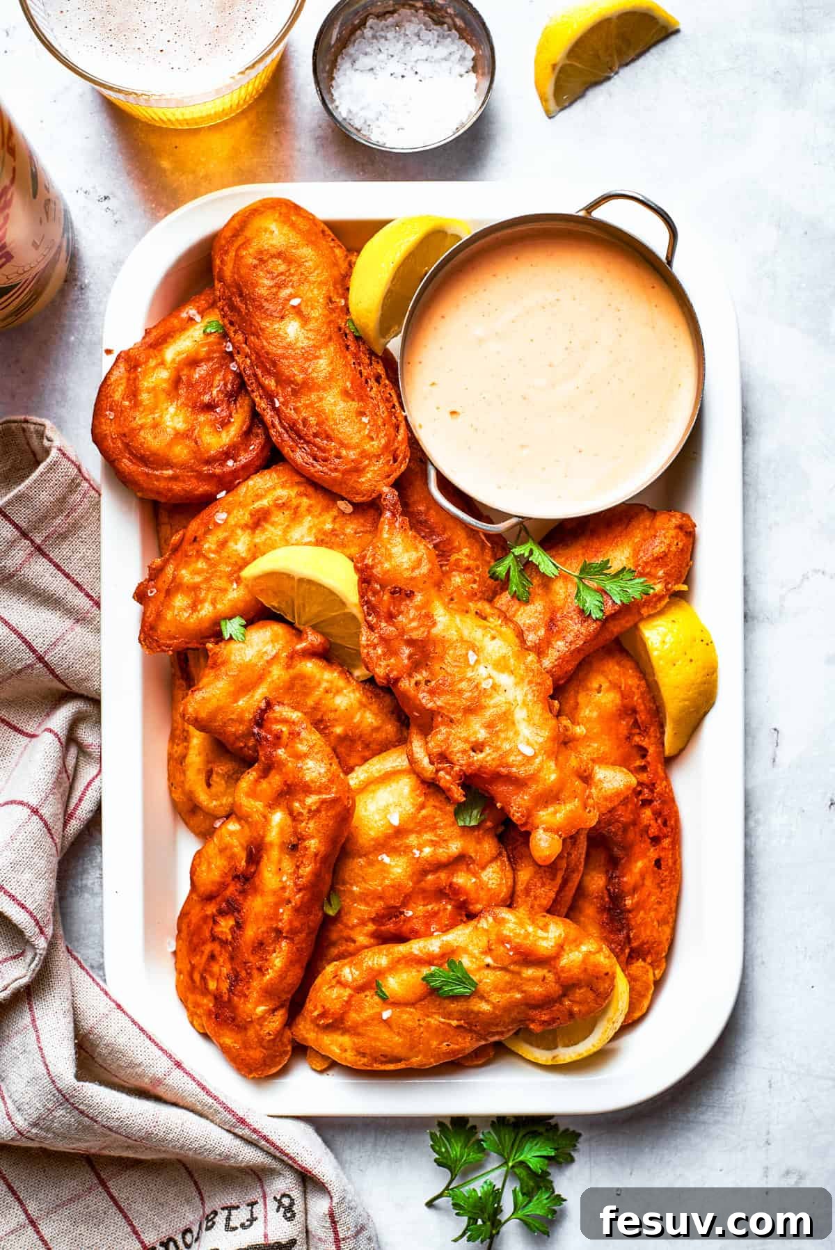 Pieces of golden, crispy beer battered chicken arranged on a rectangular serving plate with a small bowl of dipping sauce.
