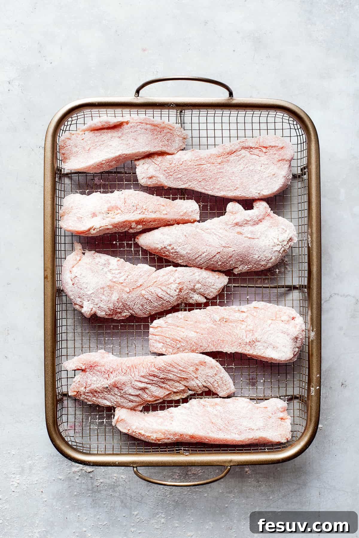 Sliced chicken pieces seasoned and arranged on a wire rack, ready for dredging.