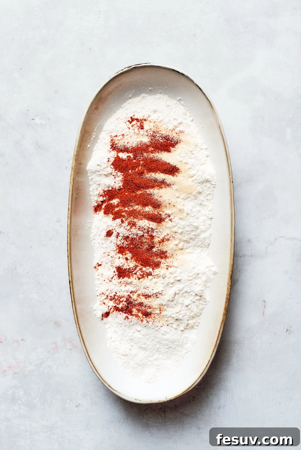 A bowl with all-purpose flour and various spices being added, forming the dredging mixture.