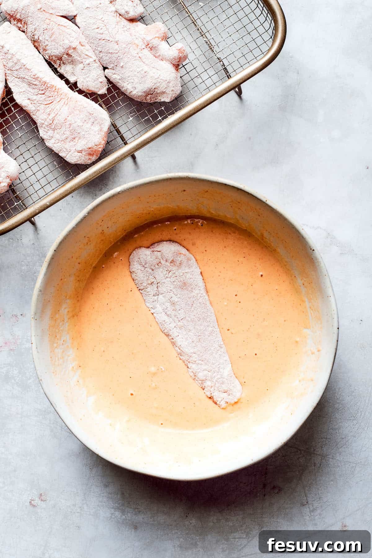 A flour-coated chicken strip being immersed into the thick, golden beer batter.