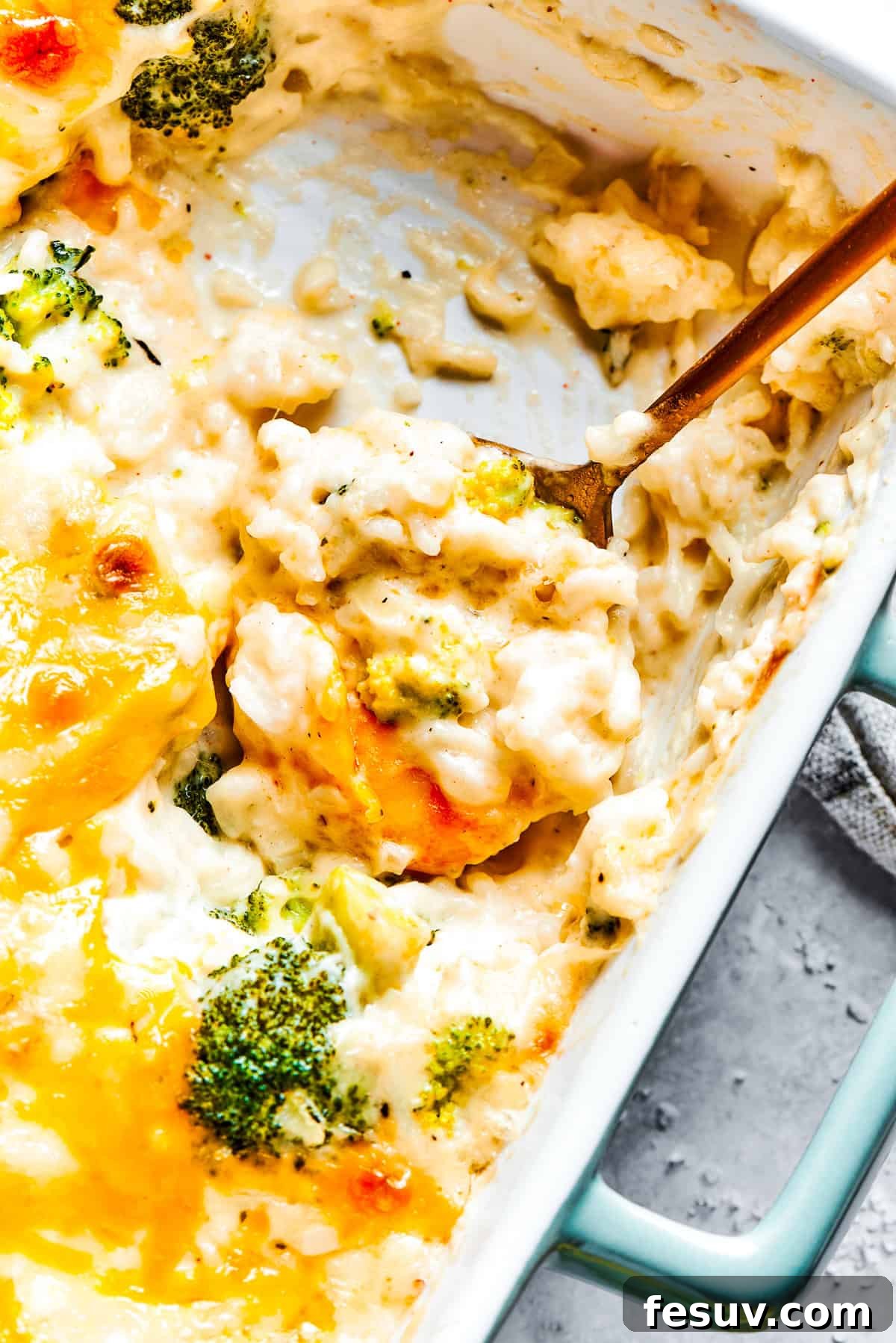 From-scratch Broccoli & Rice Casserole folds tender broccoli and fluffy white rice into a gorgeously creamy three-cheese sauce. A serving utensil scoops into a pan of broccoli & rice casserole.