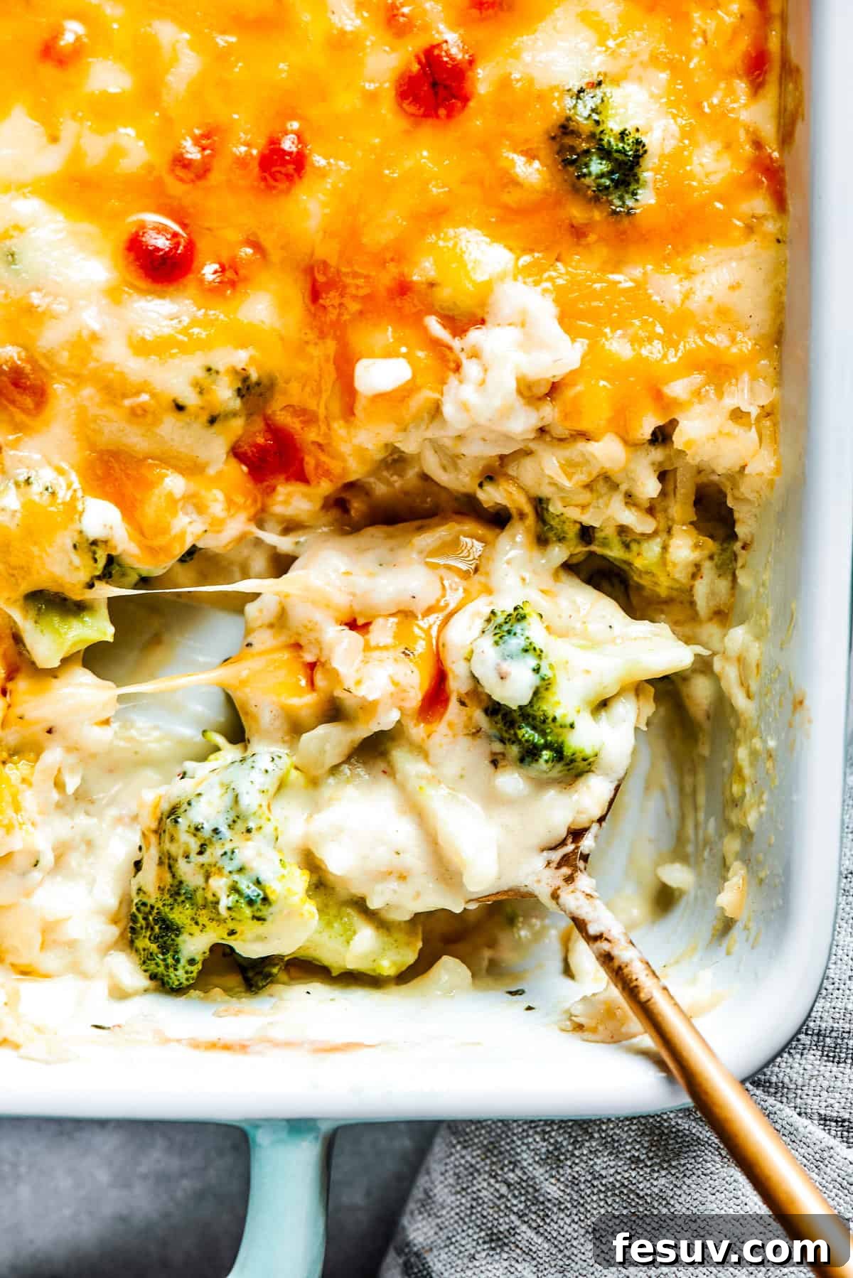 From-scratch Broccoli & Rice Casserole folds tender broccoli and fluffy white rice into a gorgeously creamy three-cheese sauce. A serving spoon scooping out broccoli rice casserole from a baking dish.