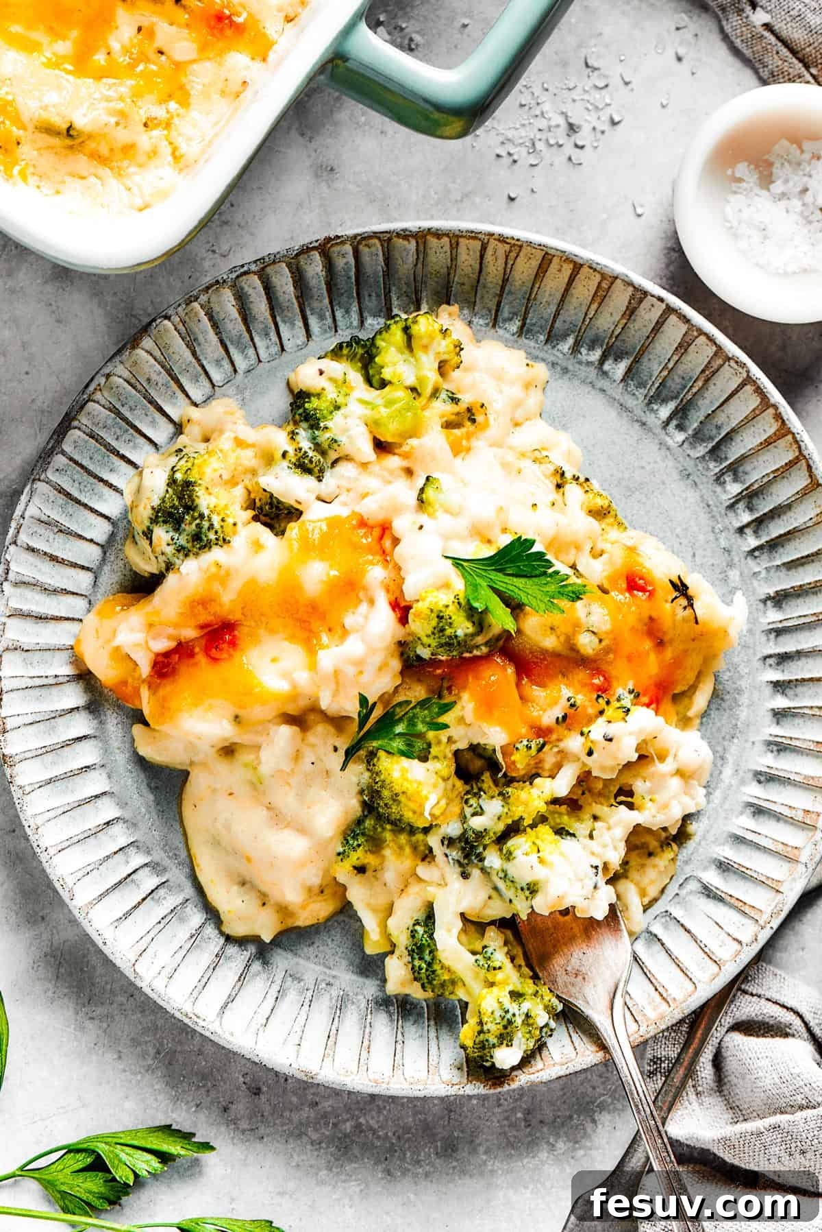 From-scratch Broccoli & Rice Casserole folds tender broccoli and fluffy white rice into a gorgeously creamy three-cheese sauce. A serving of broccoli & rice casserole on a blue plate with a fork.