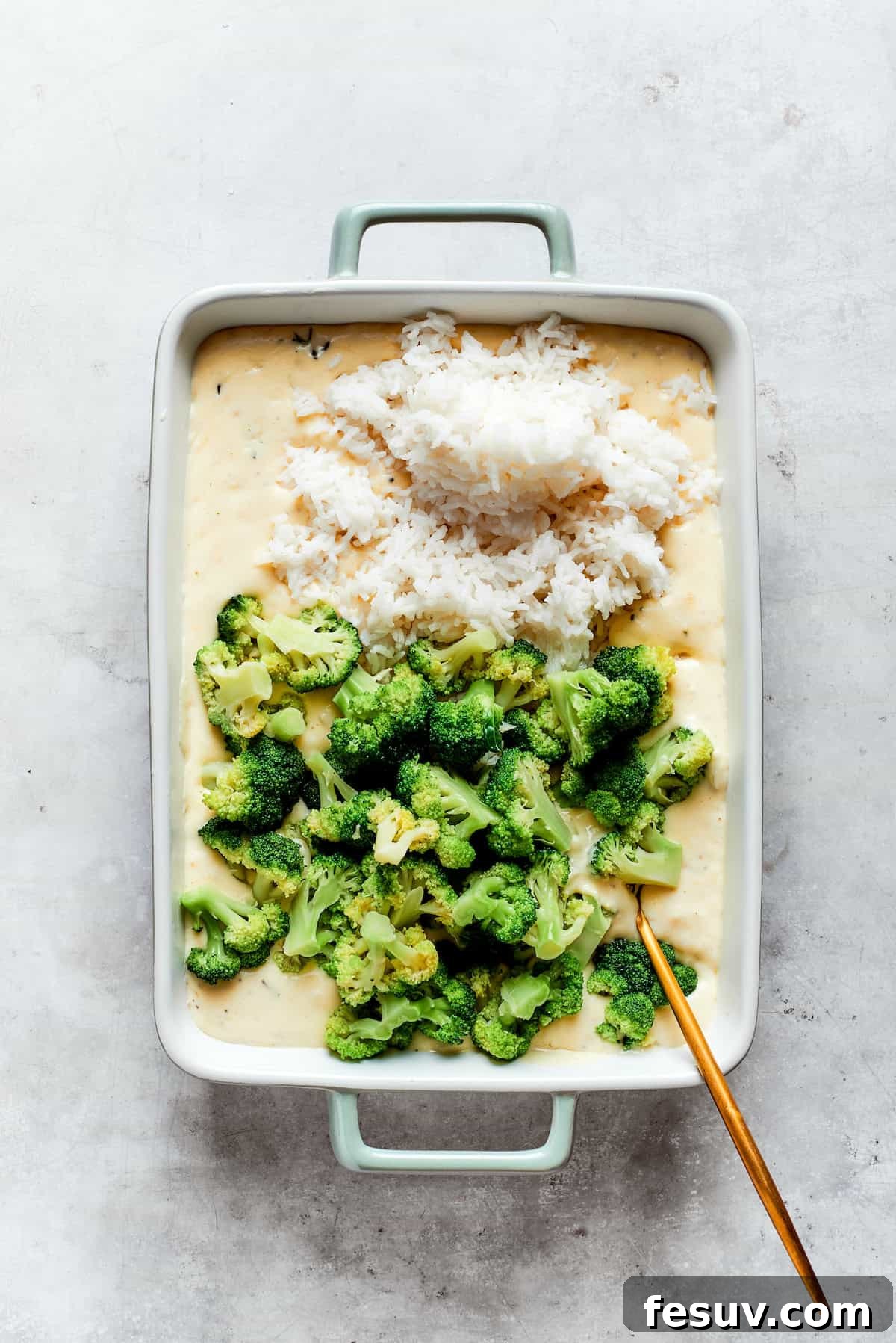 From-scratch Broccoli & Rice Casserole folds tender broccoli and fluffy white rice into a gorgeously creamy three-cheese sauce. A baking pan with cheese sauce, broccoli, and rice.