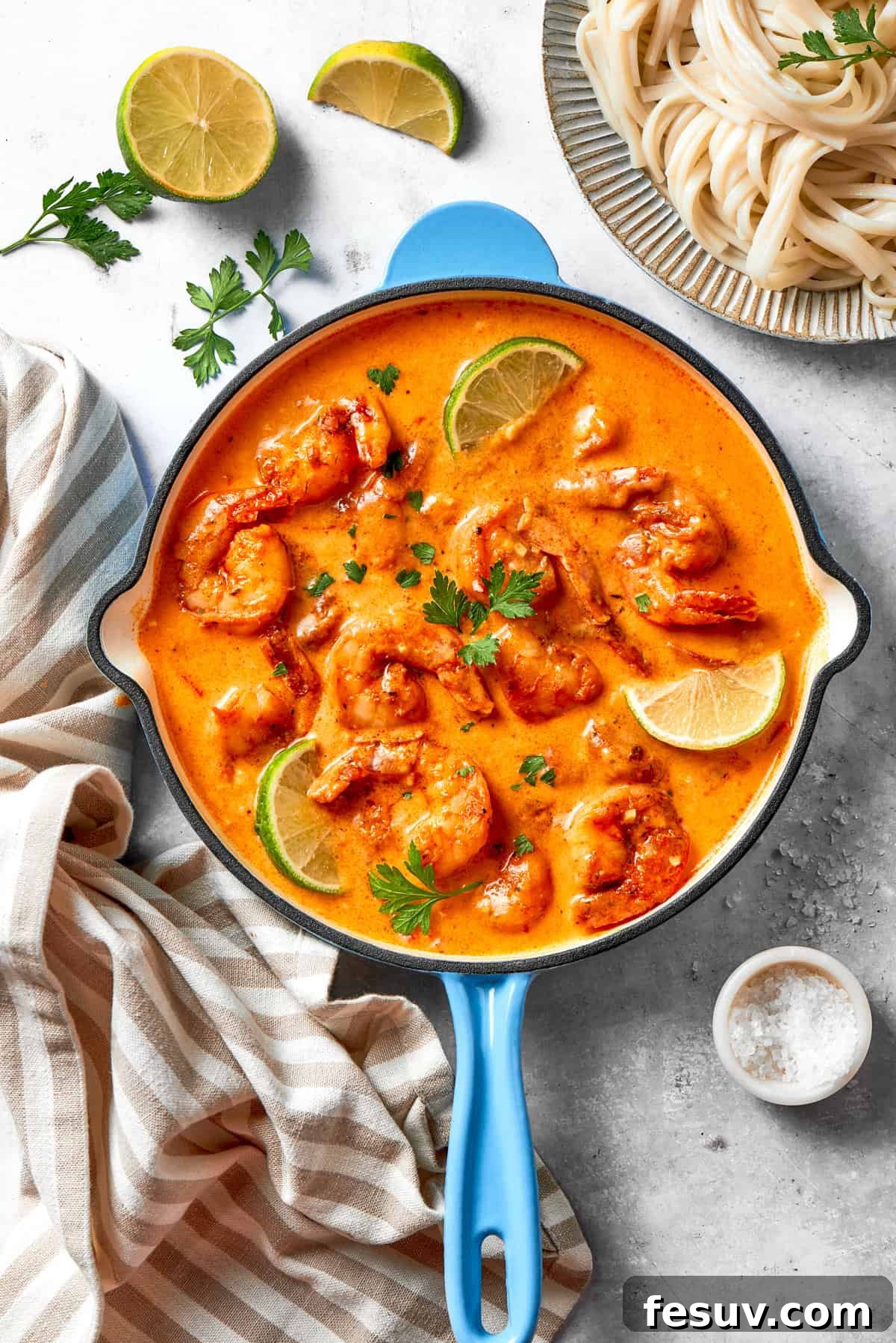 A skillet of cajun shrimp in tomato sauce, with lime wedges placed around the shrimp and a garnish of fresh herbs.