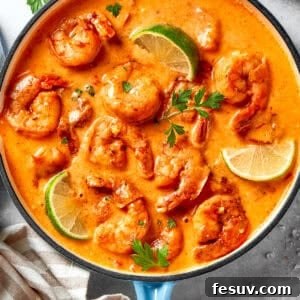 A skillet of cooked shrimp in tomato sauce. There are lime wedges arranged all around the shrimp.
