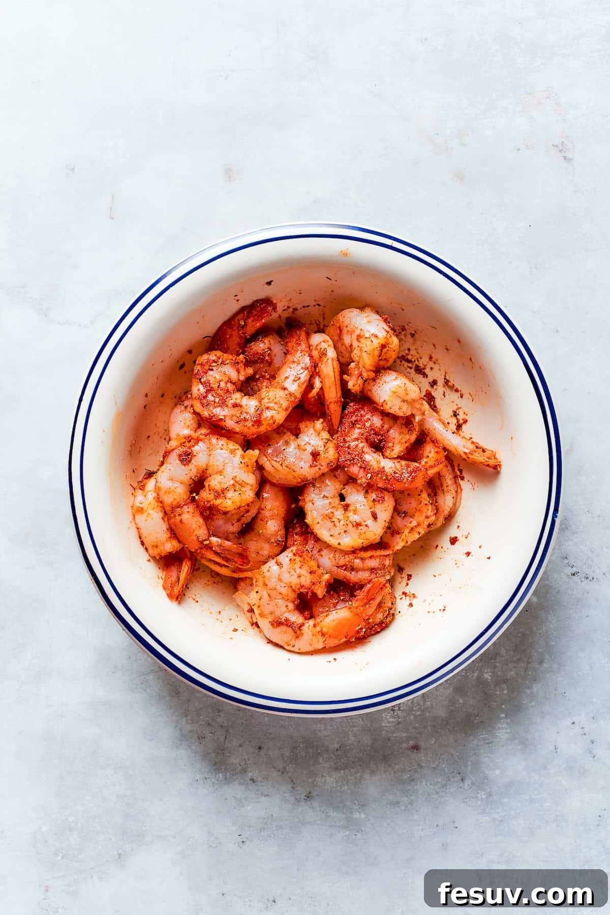 Shrimp is mixed with spices in a bowl.