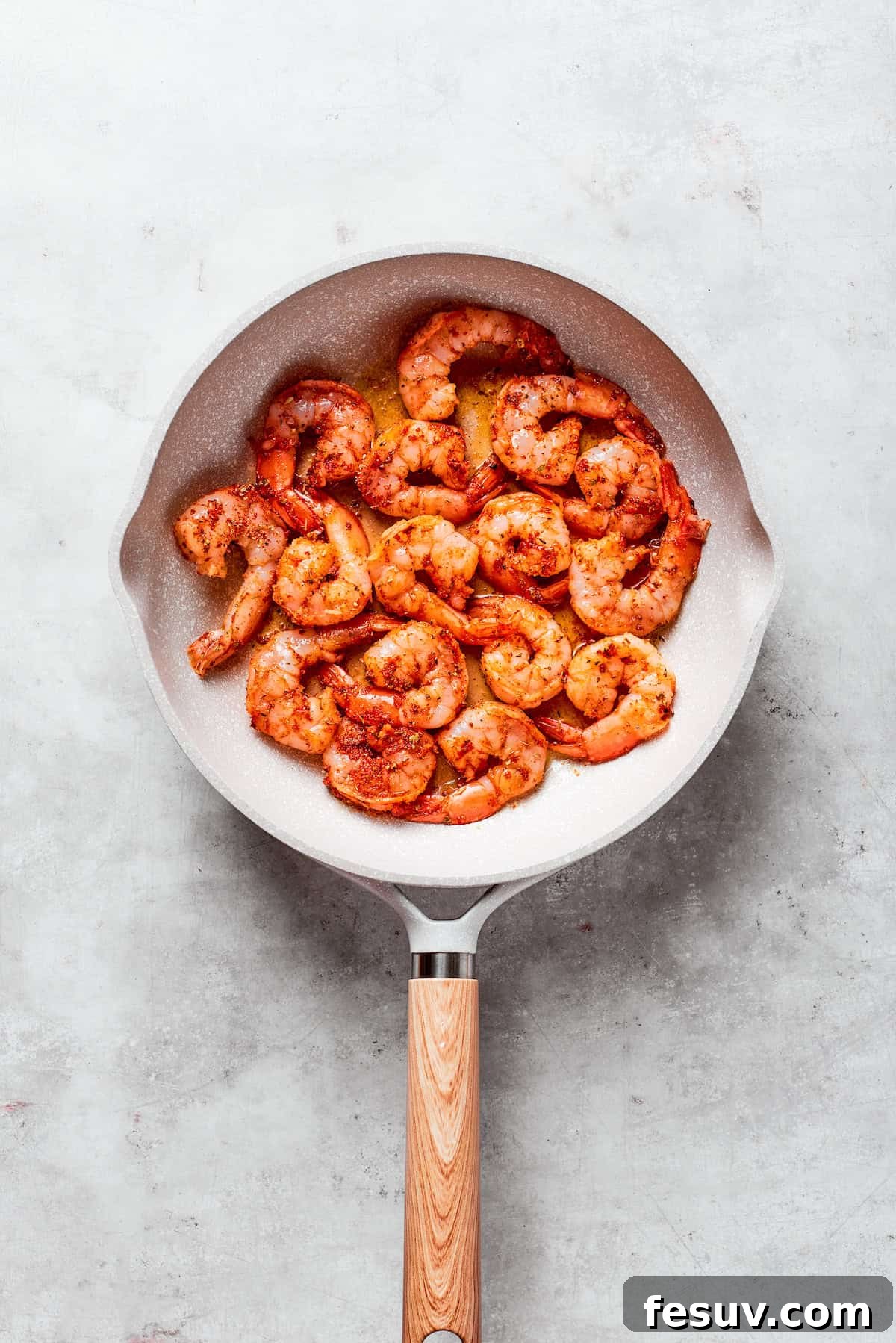 Seasoned shrimp cooks in a skillet.