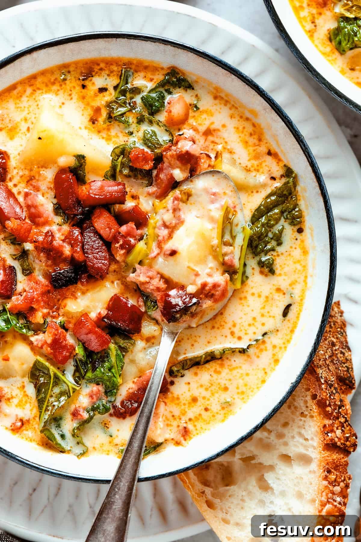 My Zuppa Toscana recipe features Italian sausage, bacon, potatoes, and kale in a savory broth. It’s an easy copycat version of the Olive Garden classic! A close-up shot of Zuppa Toscana served in a rustic bowl, with a spoon nestled inside, highlighting the rich, creamy texture and visible ingredients.