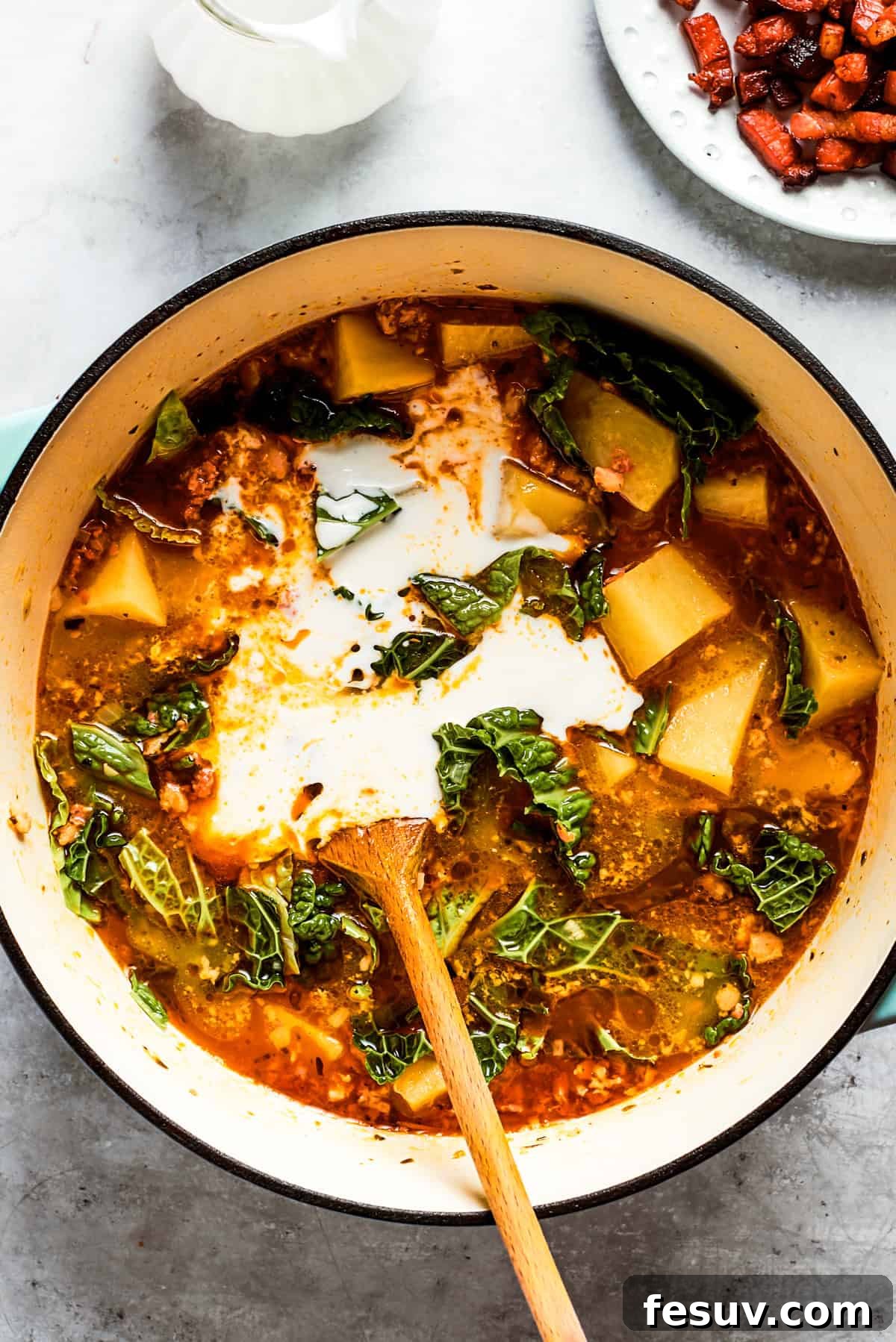 My Zuppa Toscana recipe combines a mix of Italian sausage and bacon, tender potatoes and chopped kale in a savory broth. A hand stirring rich heavy cream into a pot of Zuppa Toscana soup, which contains diced potatoes, sausage, and kale.