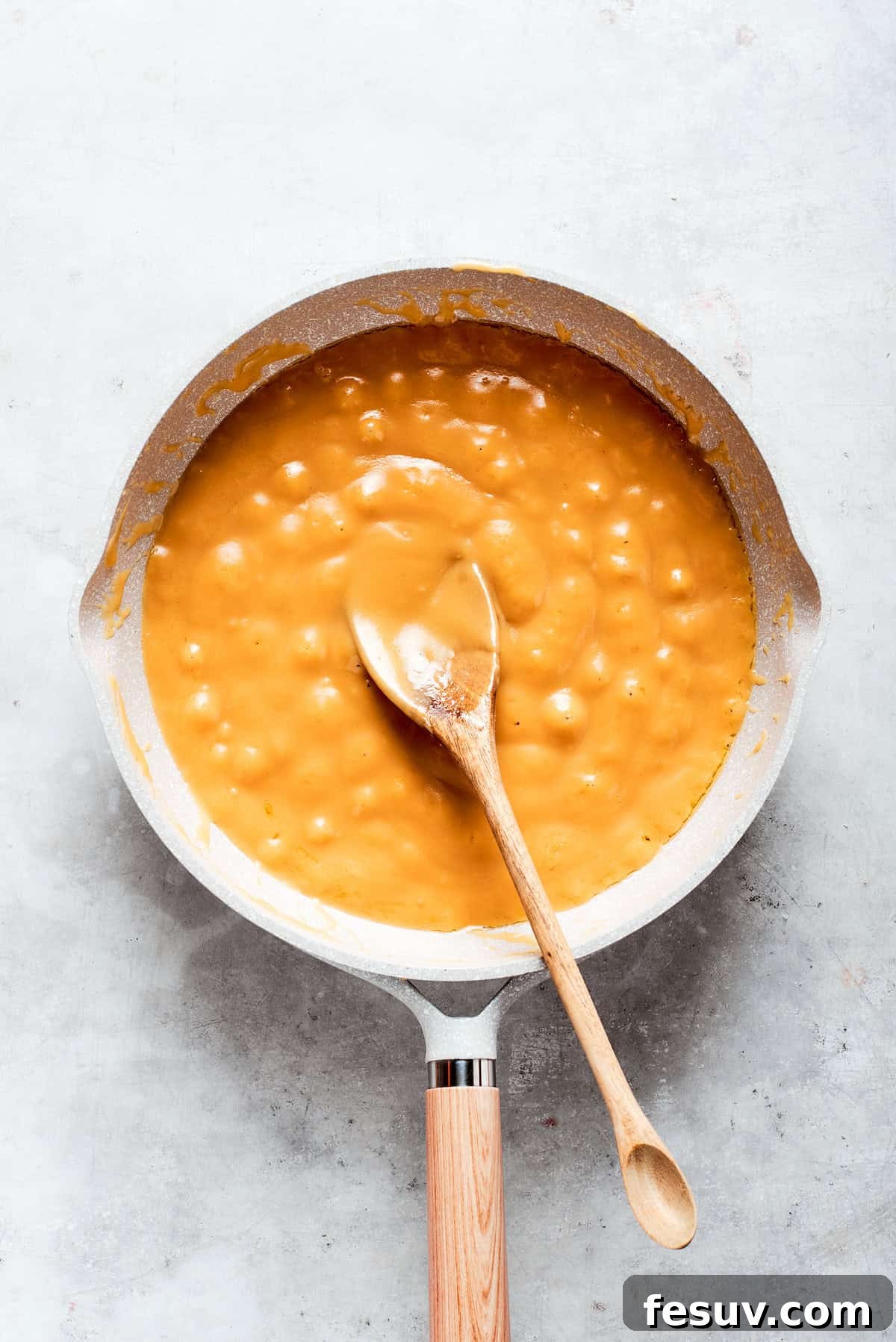 Caramel sauce is stirred until smooth and thick in a pot.