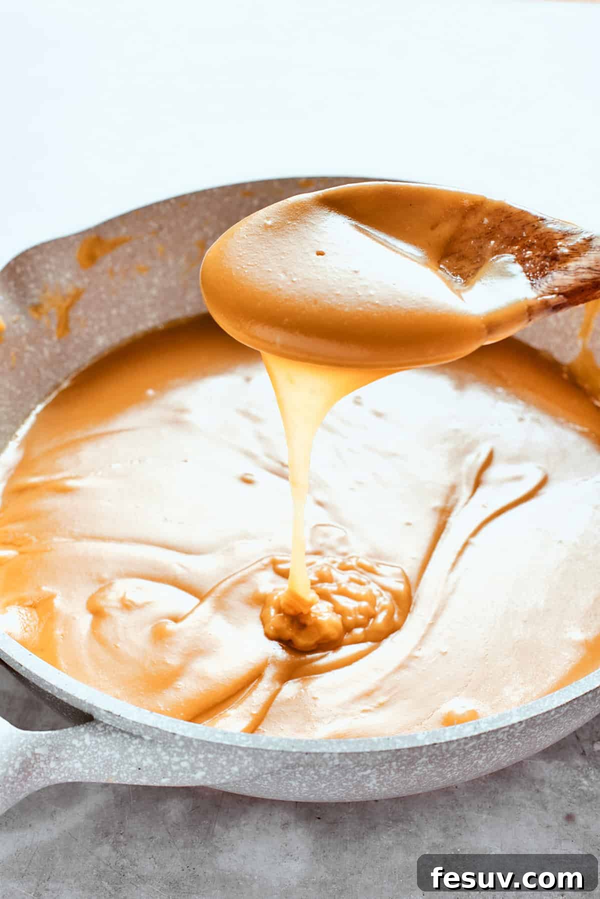 A spoon lifts up some golden caramel sauce, showing its thick consistency.